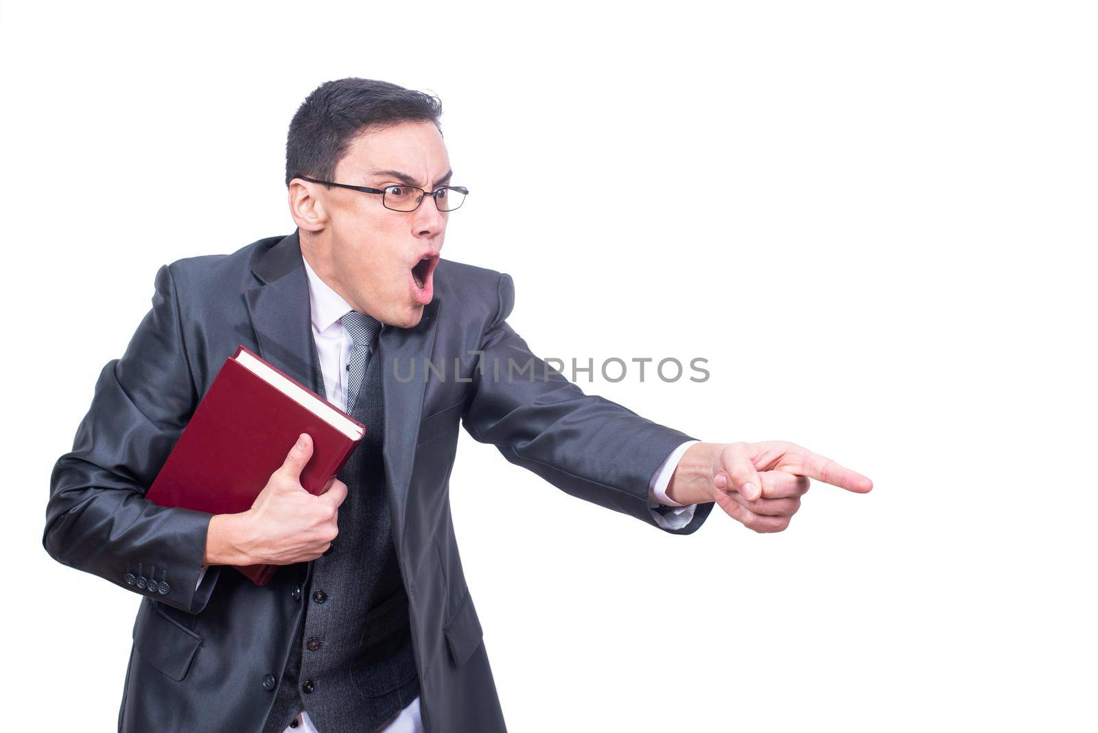 Furious male teacher in formal suit and eyeglasses with book pointing away while swearing isolated on white background in light studio