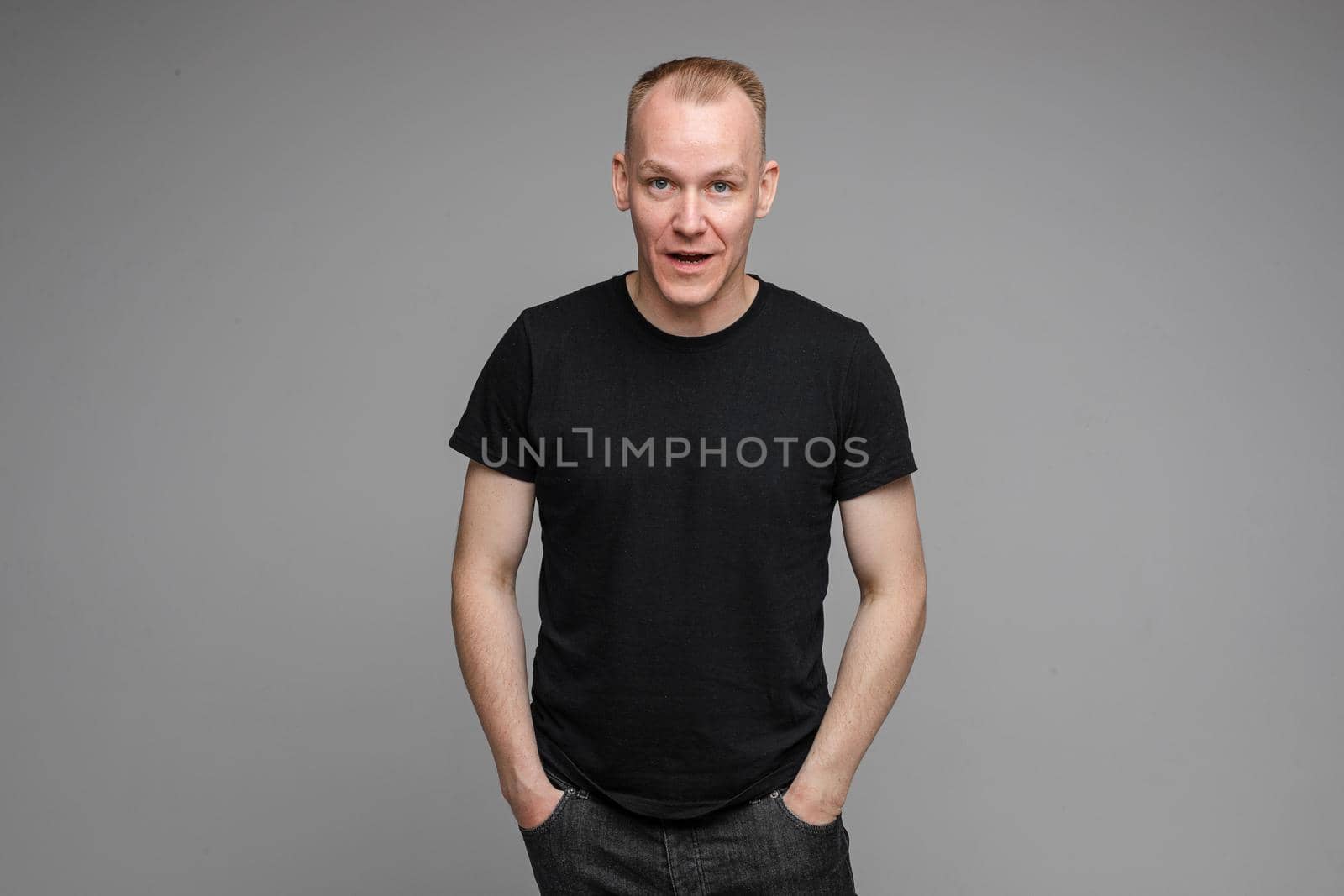 picture of handsome caucasian male keeps hands together looks with surprised sight isolated on grey background