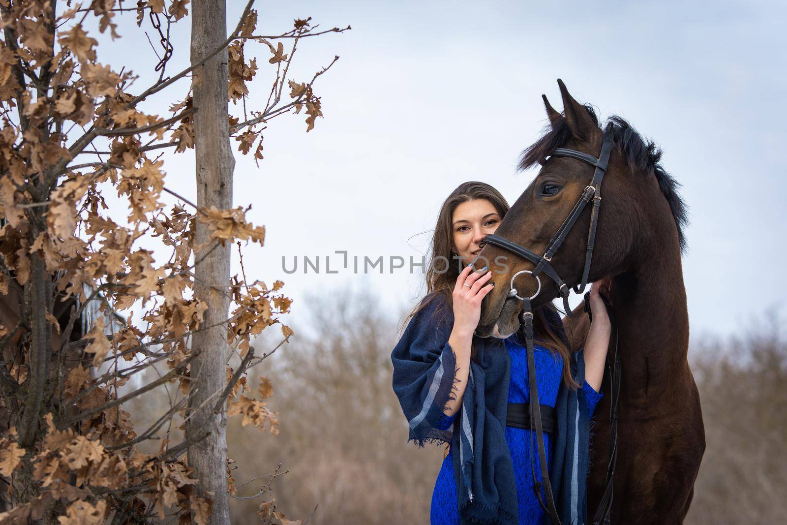 The girl peeks out from behind the muzzle of a horse, in the background an autumn forest a