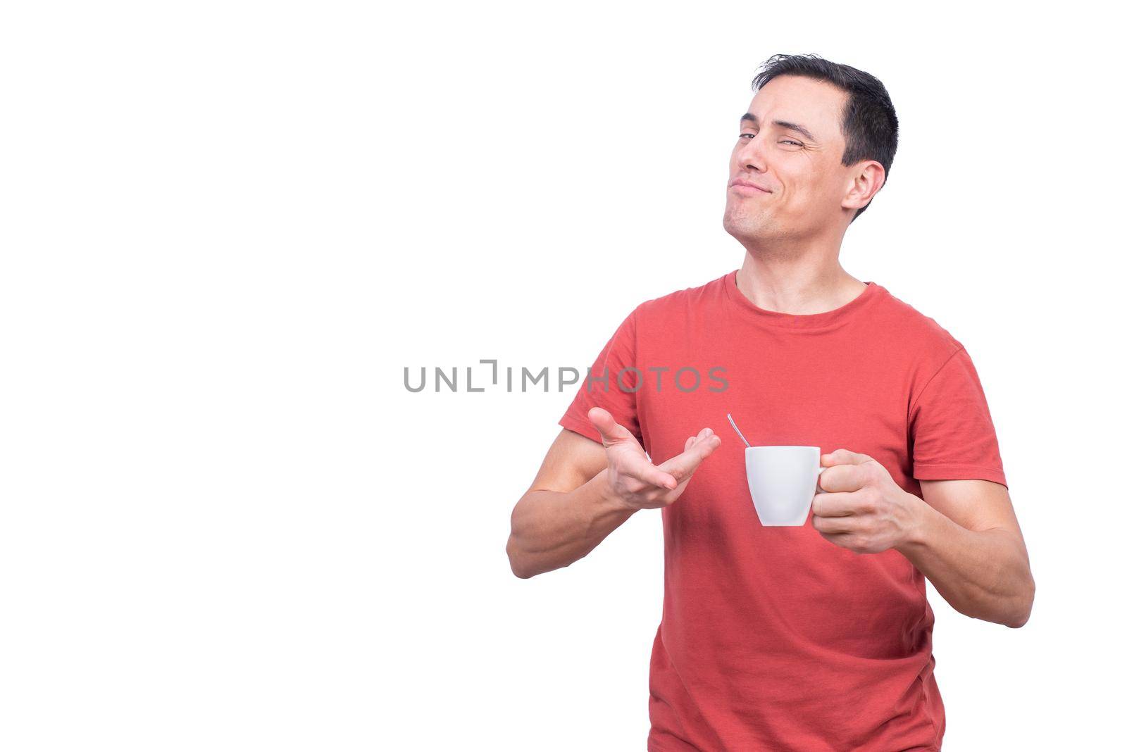 Pleased guy in red shirt holding cup of hot coffee and looking at camera against white background