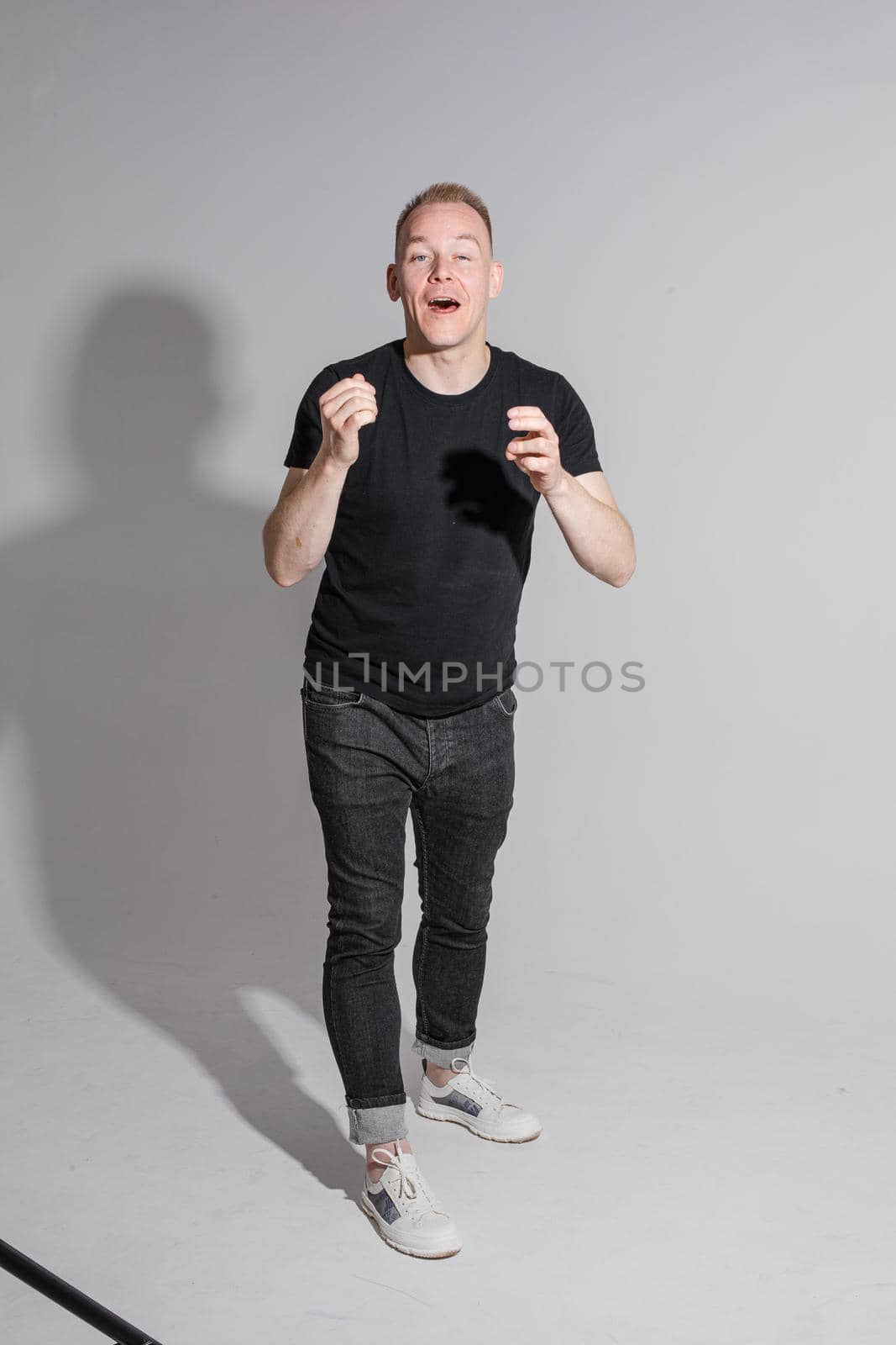 Full-length photo of man in black clothes raising his hands and opening mouth while posing at studio