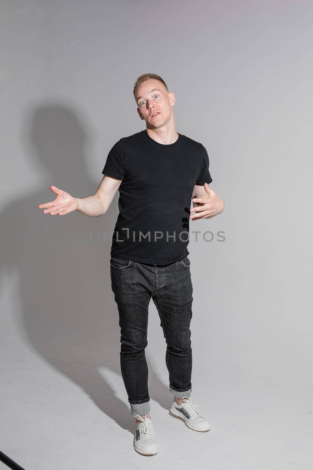 funny man keeping his hands up and smiles in studio on white background, backstage of a photosession