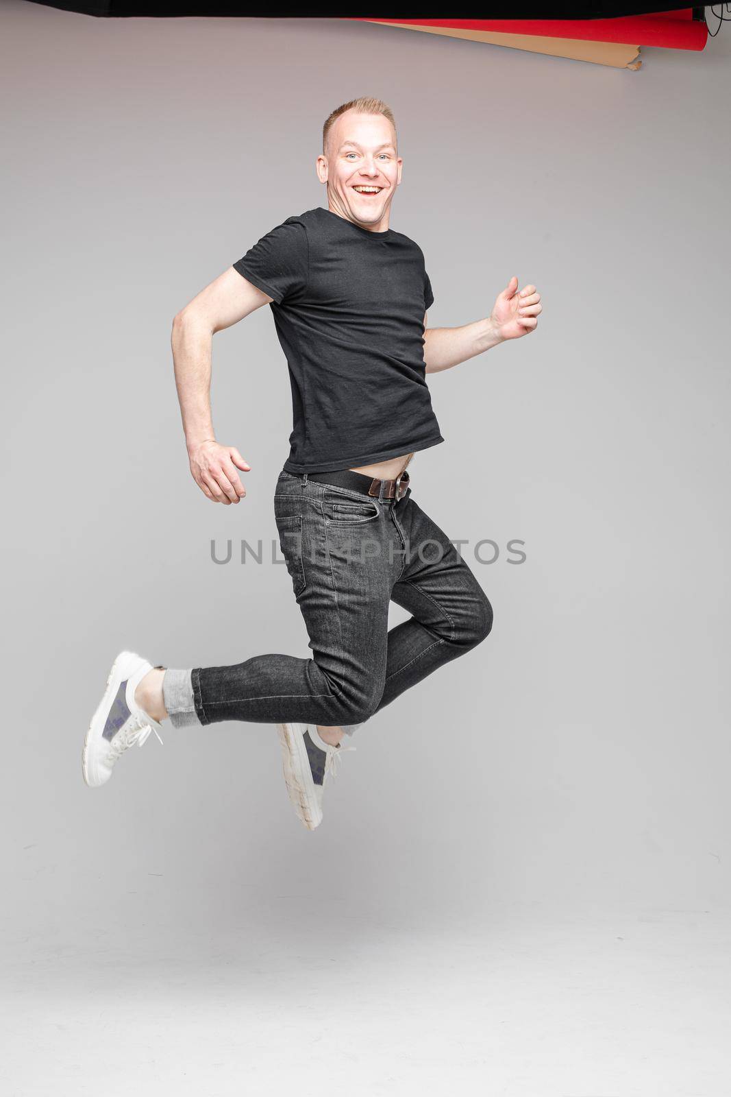 funny man jumps and rejoices in studio on white background, backstage of a photosession by StudioLucky