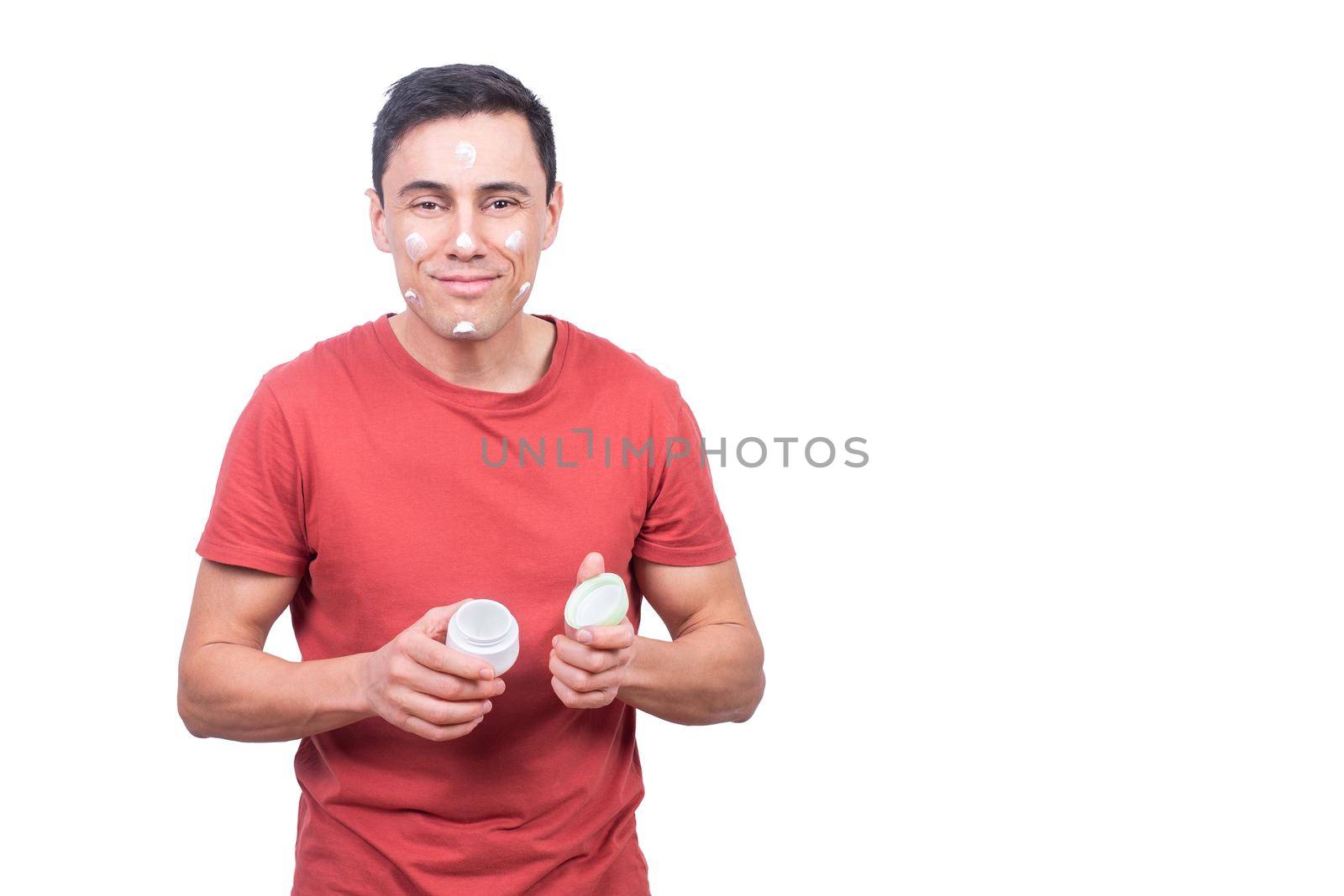 Positive male with anti aging facial cream looking at camera with smile during daily skin care routine isolated on white background