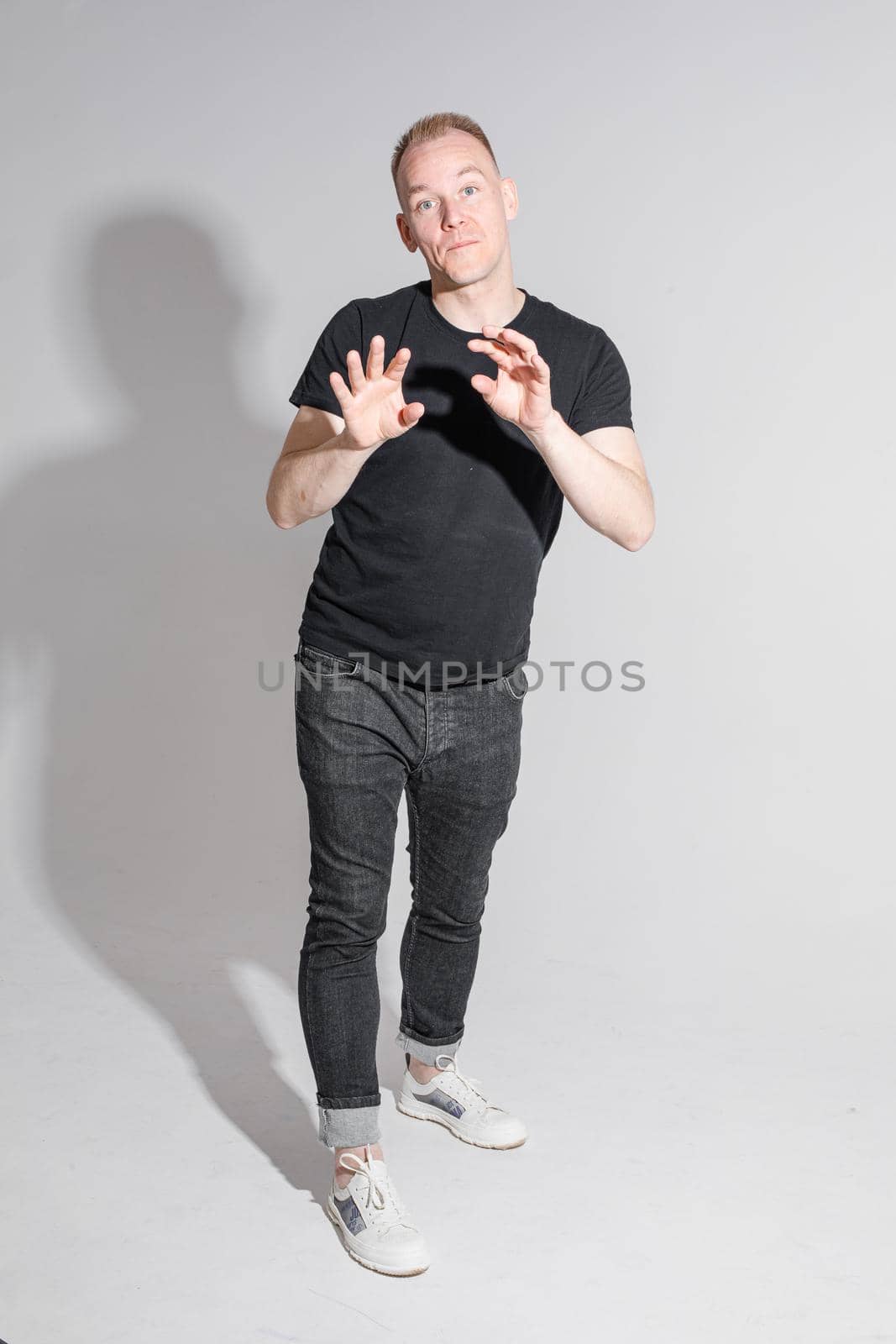 Full-length photo of man in black clothes raising his hands and opening mouth while posing at studio