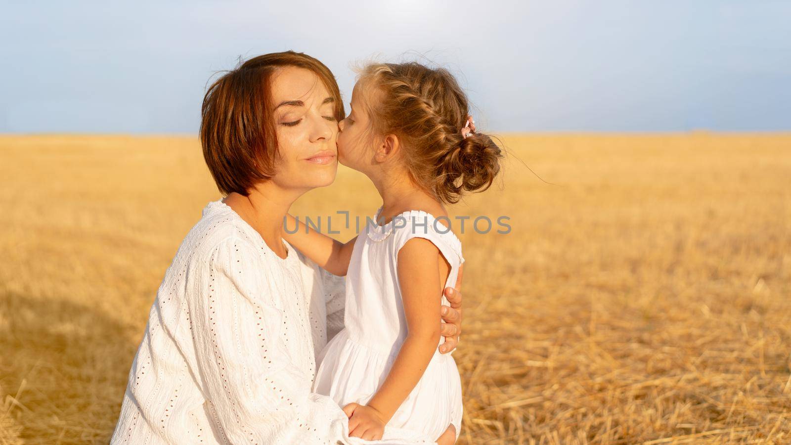 Daughter kisses her mom cheek standing wheat field by andreonegin