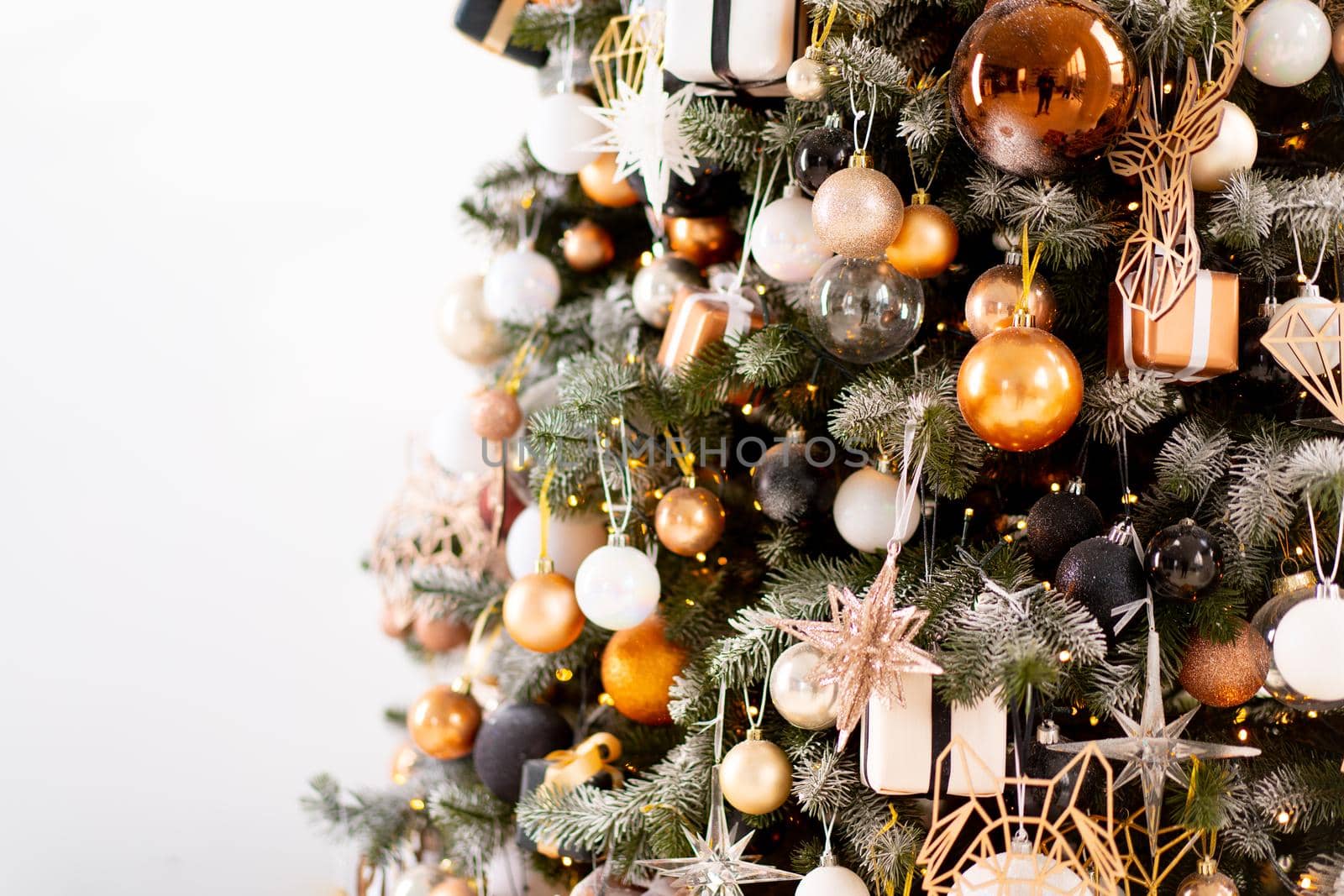 Christmas tree close up standing white wall background decorated white black gold color with light garland. Christmas decoration with copy space