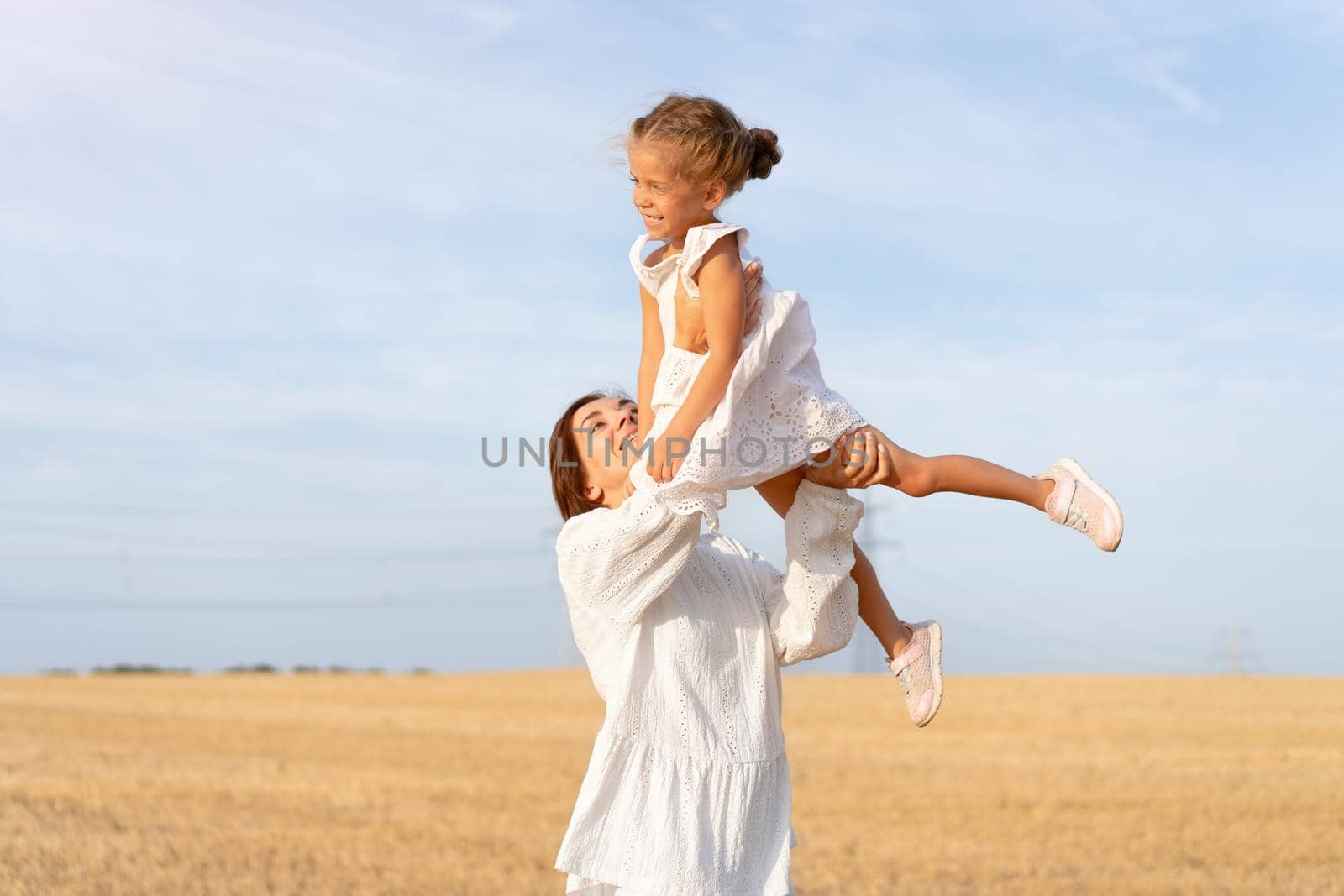 Mother throws up little daughter in air standing wheat field summer day blue sky background by andreonegin