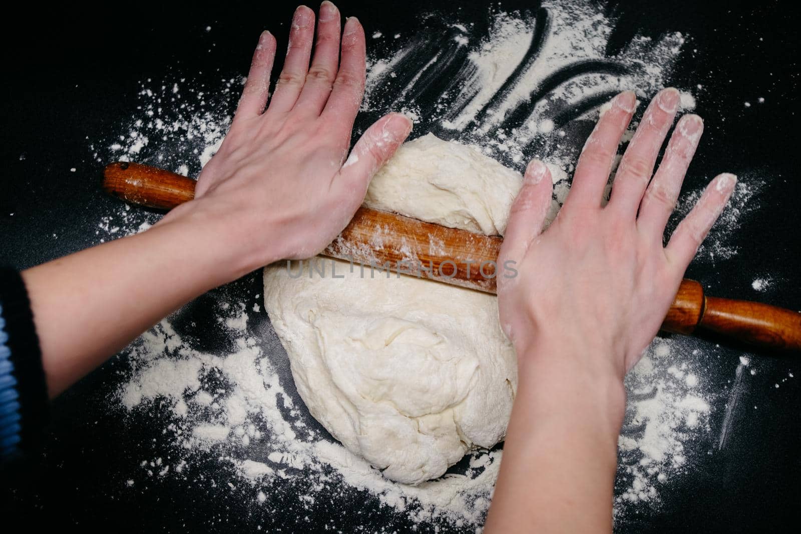 Pizza dough on a black table with hands and light