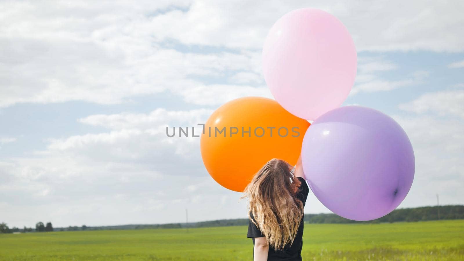 Happy girl with big multicolored balloons posing on the field