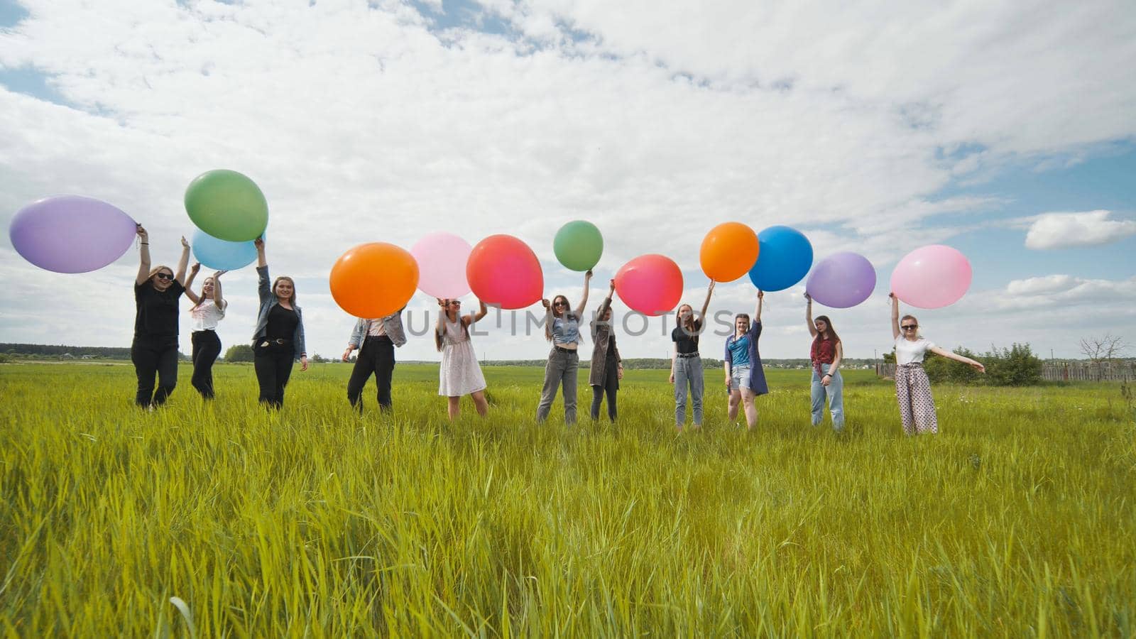 Cheerful girls are standing on the field with large balloons and colorful balloons