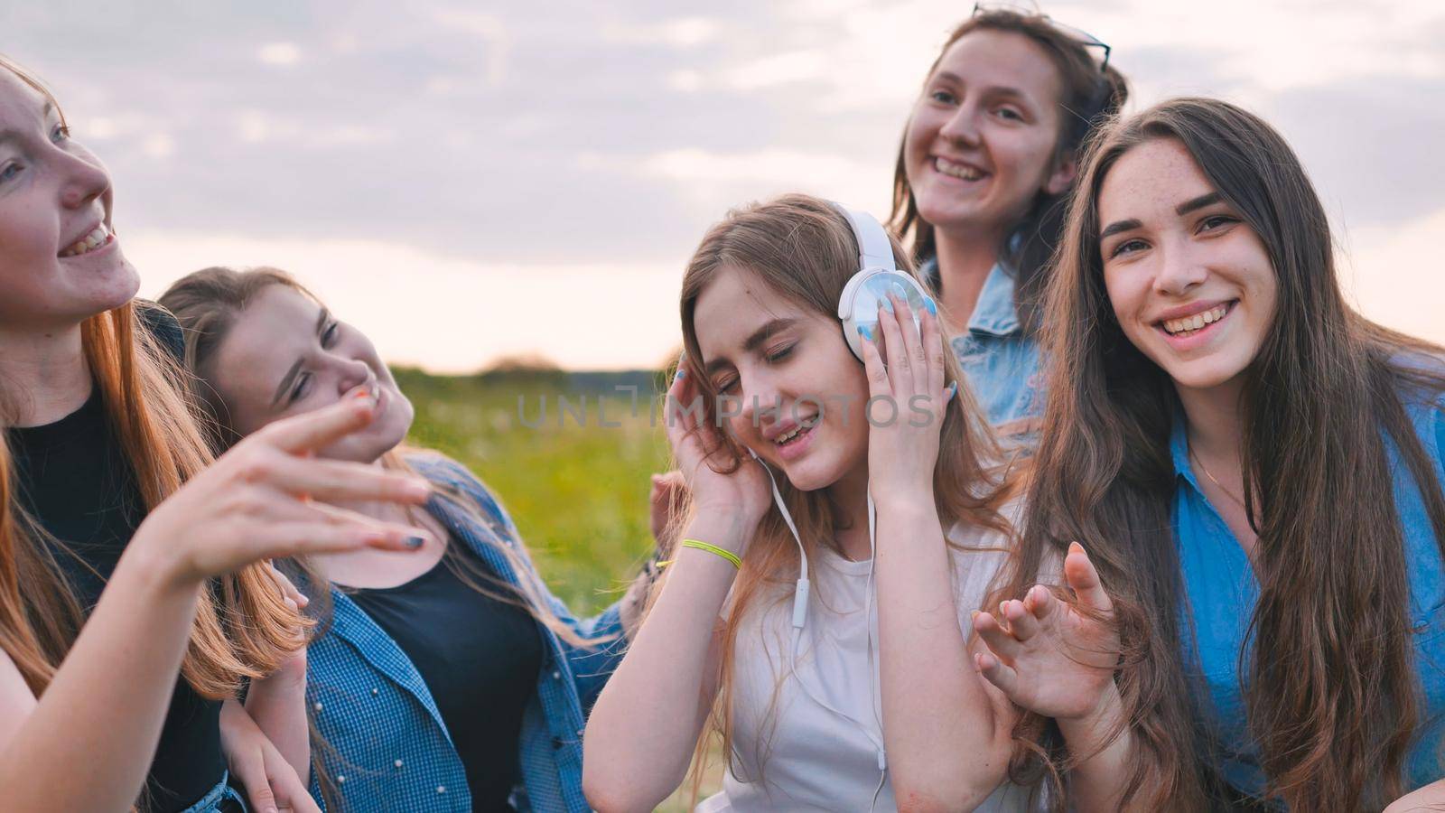 A group of girls of friends are listening to music on headphones and dancing to a friend