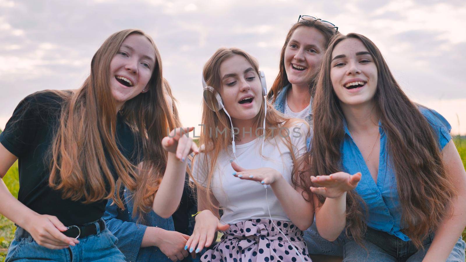 A group of girls of friends are listening to music on headphones and dancing to a friend. by DovidPro