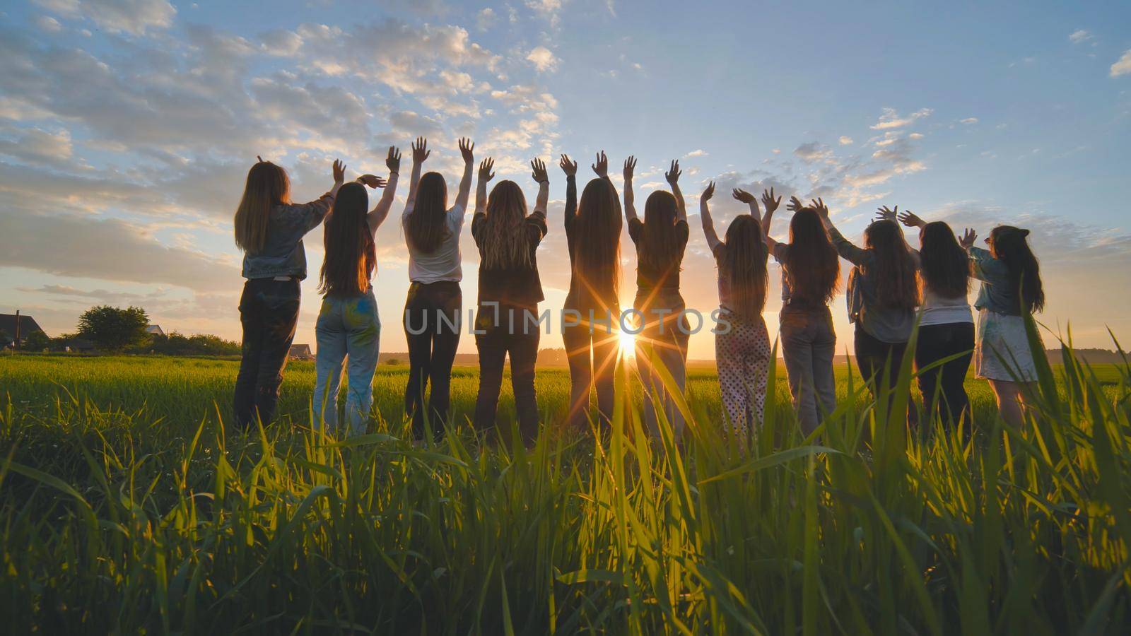 Silhouette of friends of 11 girls waving their hands at sunset in the field