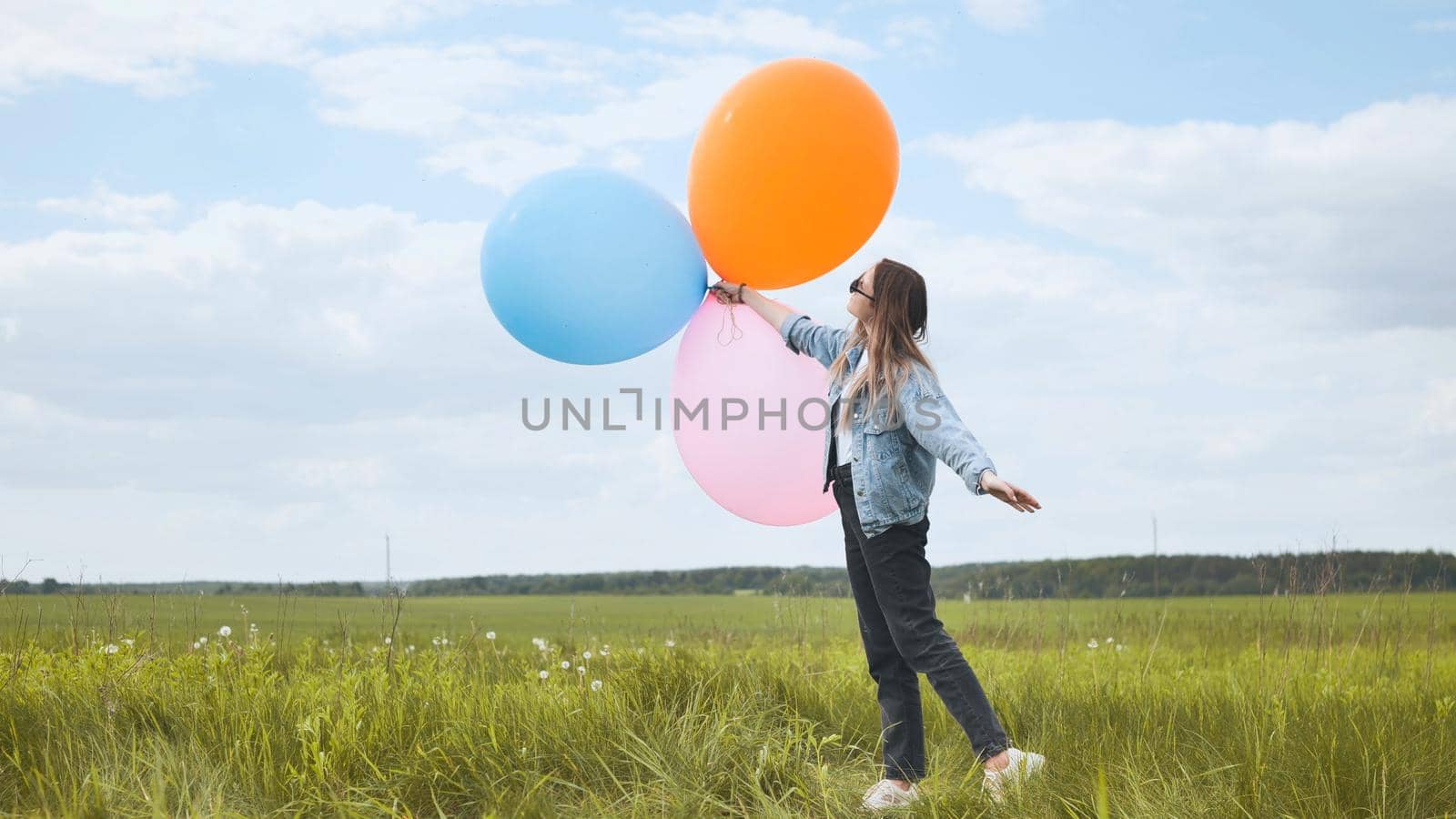 Happy girl with big multicolored balloons posing on the field