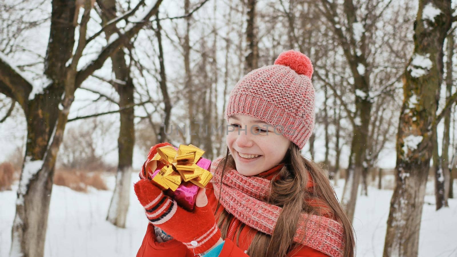A beautiful young schoolgirl standing in a snowy forest in the winter takes a joyful gift from the hands of a friend