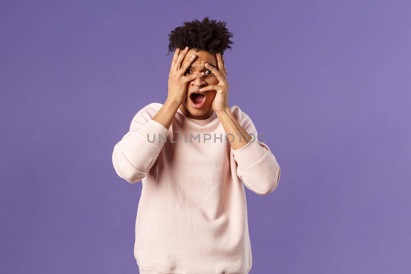 Portrait of shocked, startled handsome man being embarrassed and scared of seeing something unappropriate and awkward, cover eyes but peeking through fingers from interest by Benzoix