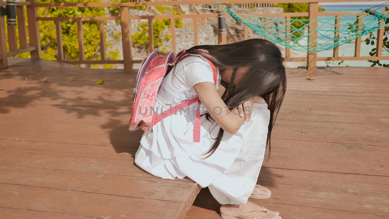 An philippine schoolgirl girl with a backpack is sitting and crying near the tropical coast. Sad mood