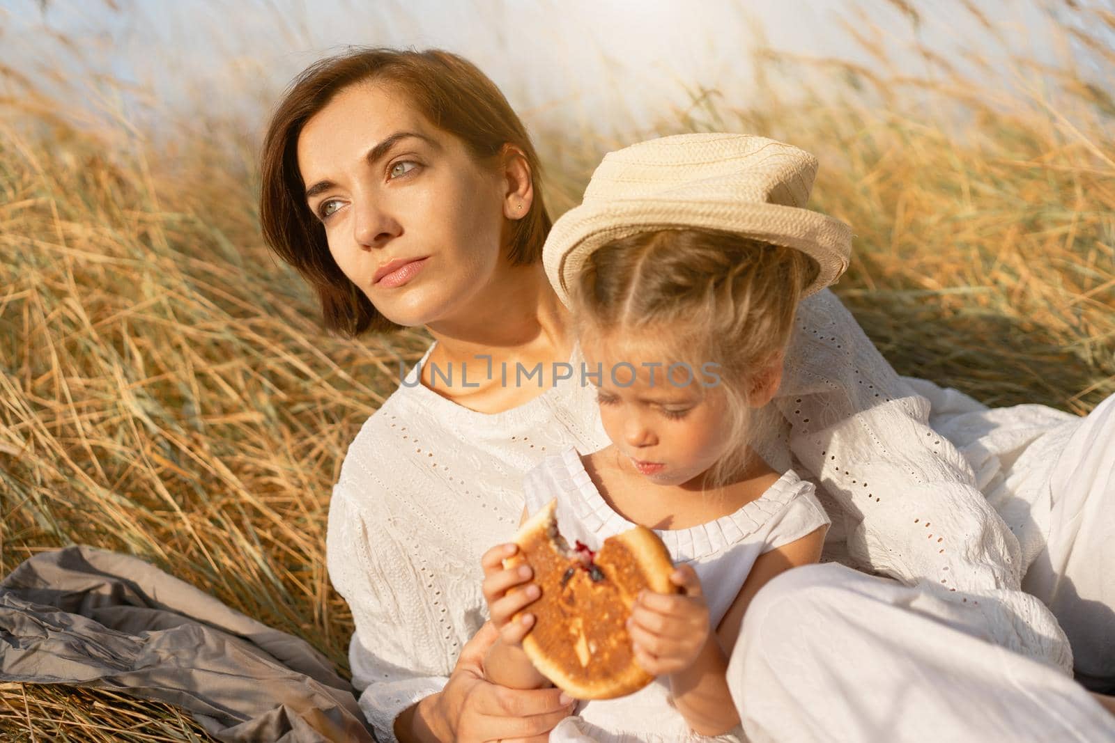 Mother and daughter sitting picnic high yellow grass child eat bun. Happy family with one child resting nature outdoor mom with little girl 5 years old. Countryside