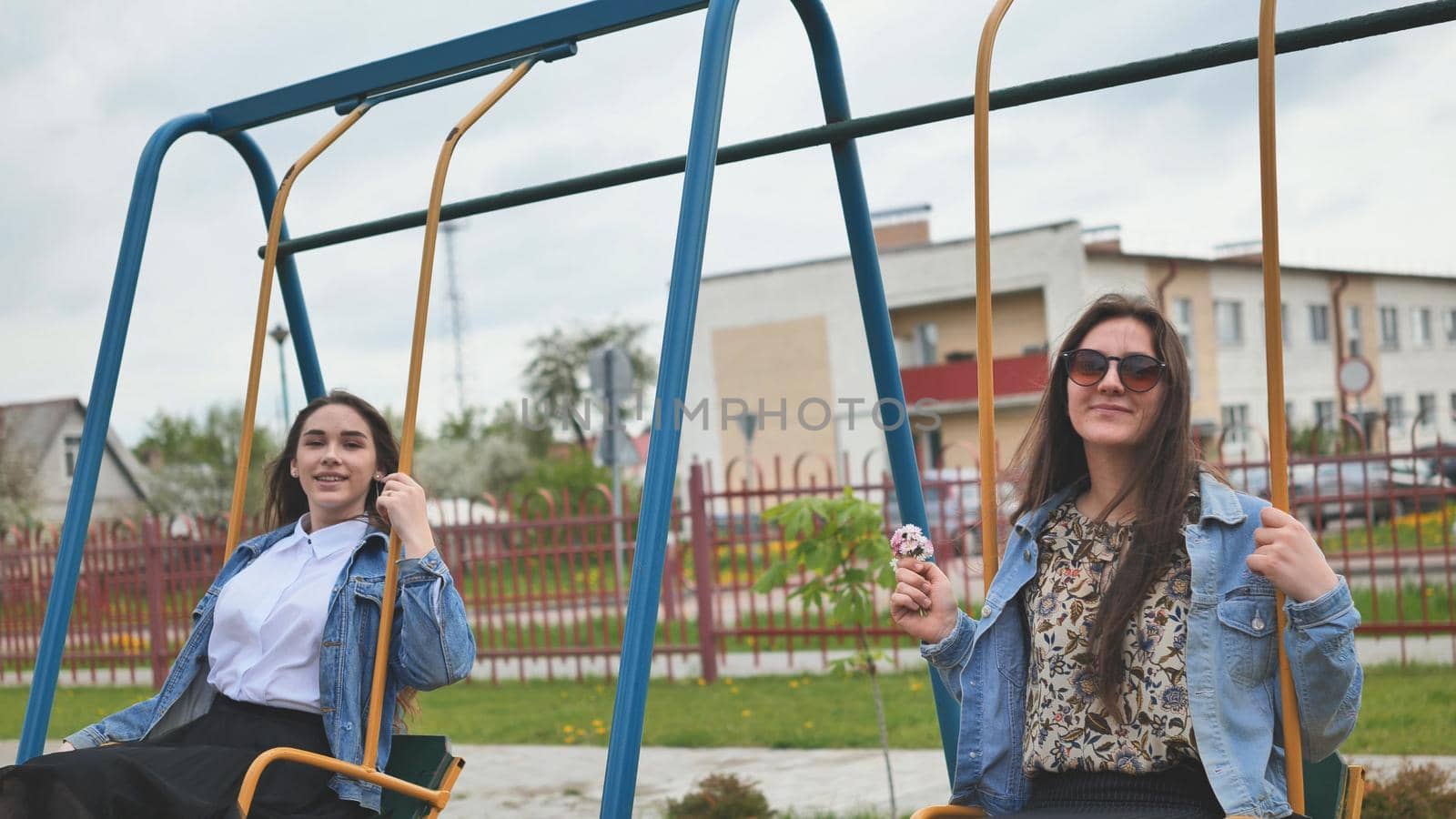 Joyful schoolgirls ride a swing in summer day. by DovidPro
