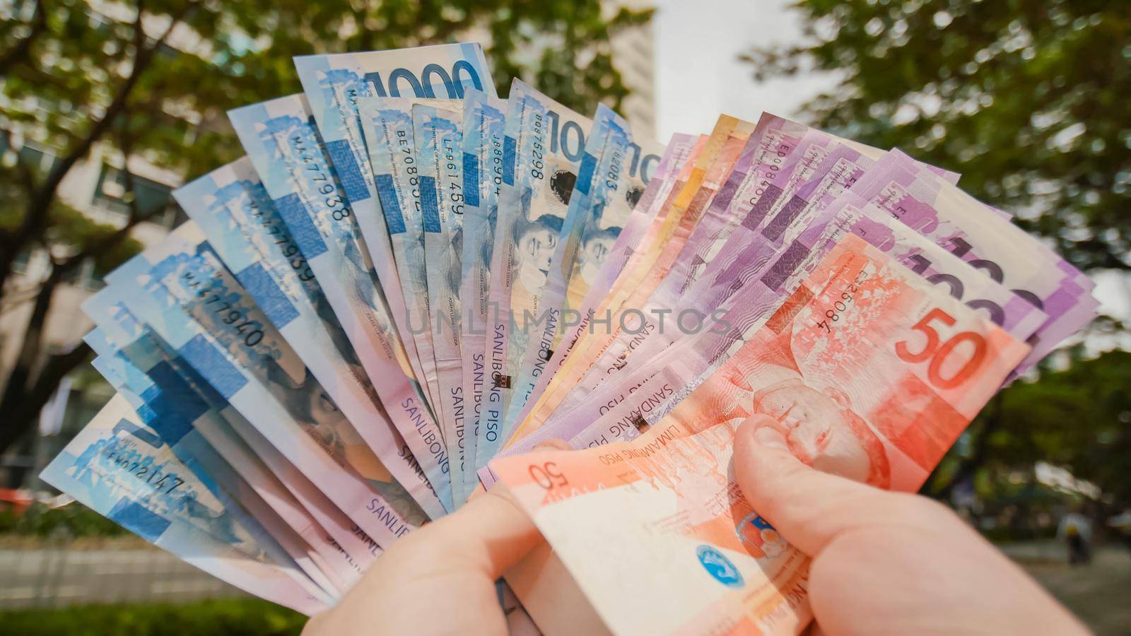 Photo of hands holding bundle of blue money in cash of one thousand philippines peso as if being rich, boastful. Show off, pay bills or give bribe. Payment procedure