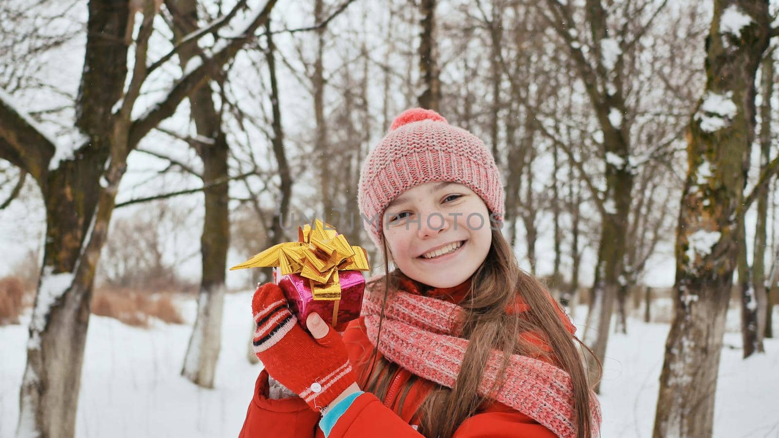 A beautiful young schoolgirl standing in a snowy forest in the winter takes a joyful gift from the hands of a friend