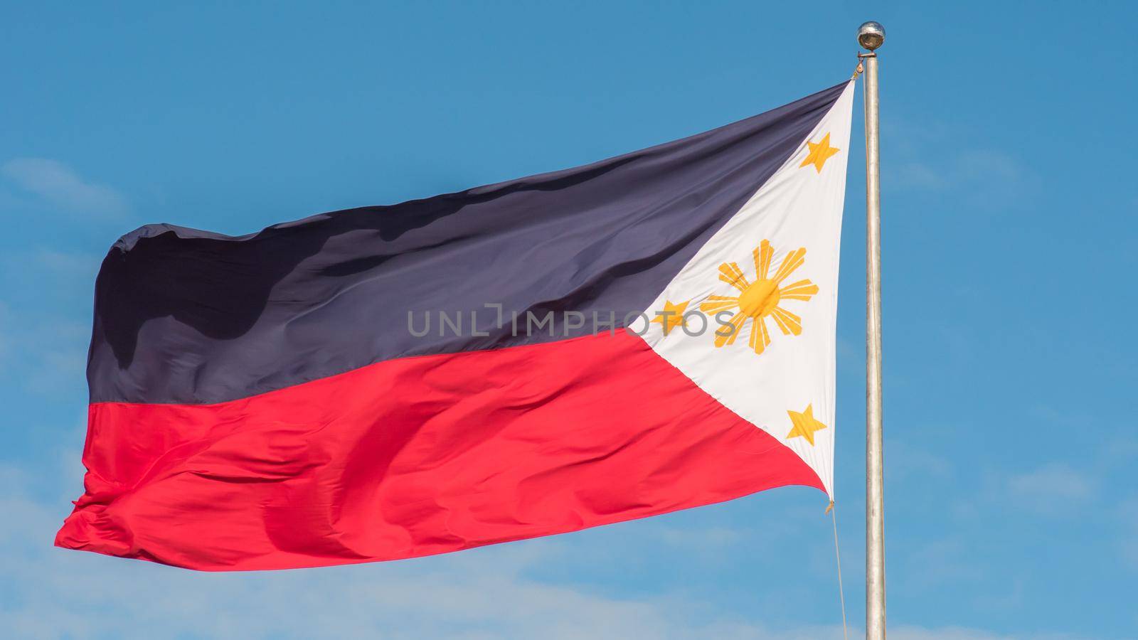 Flying bicolor flag of the Philippines with central golden sun representing the provinces and stars the islands