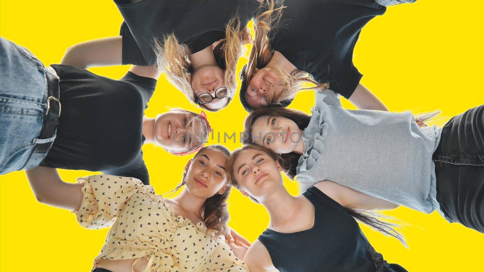 Happy girls friends hugging in a circle on a yellow background. Teamwork concept. by DovidPro