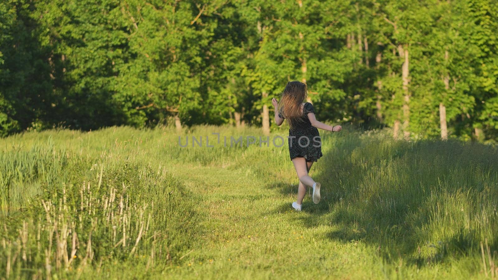 A young girl runs in a meadow on a warm summer evening