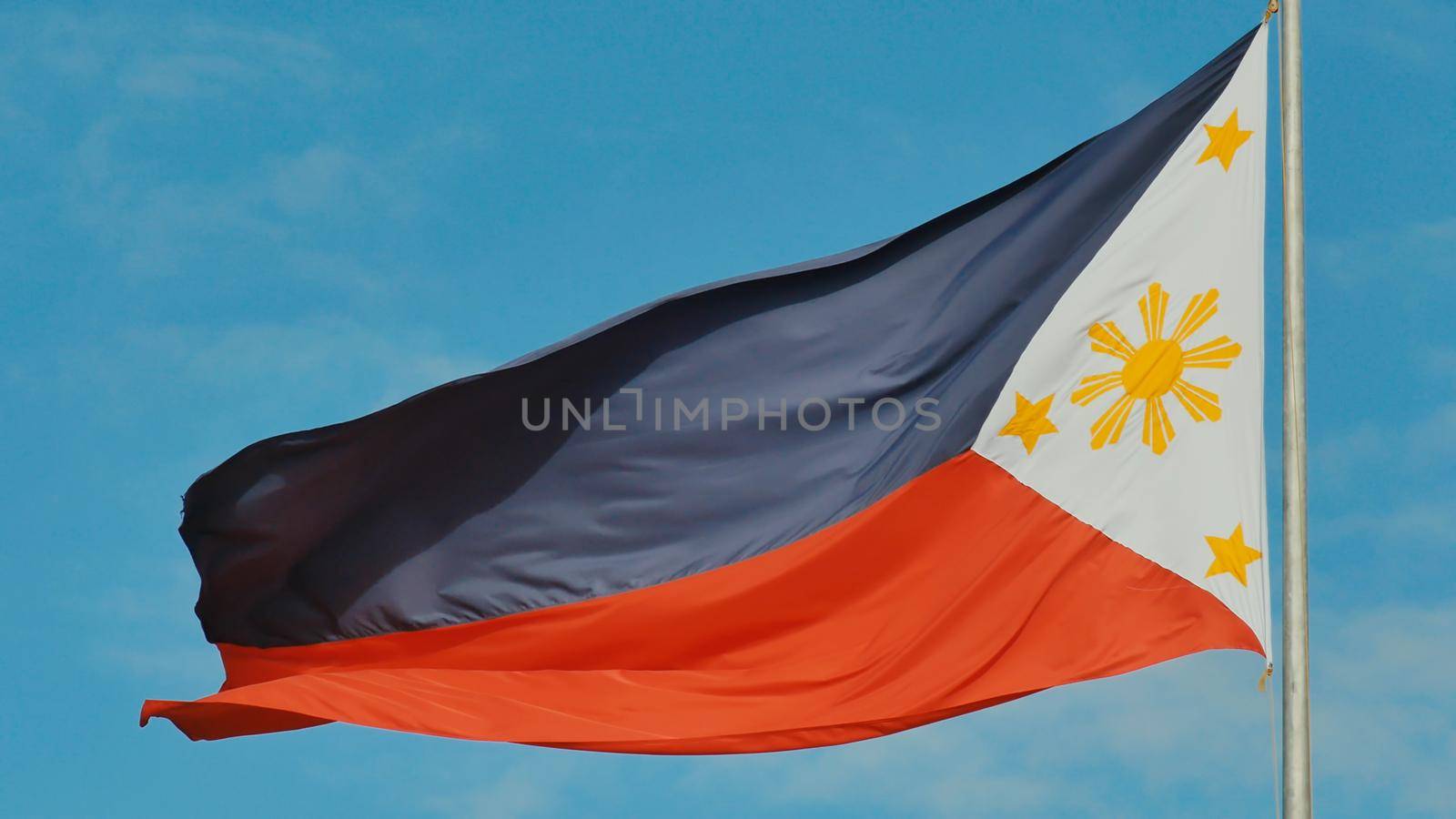 Flying bicolor flag of the Philippines with central golden sun representing the provinces and stars the islands