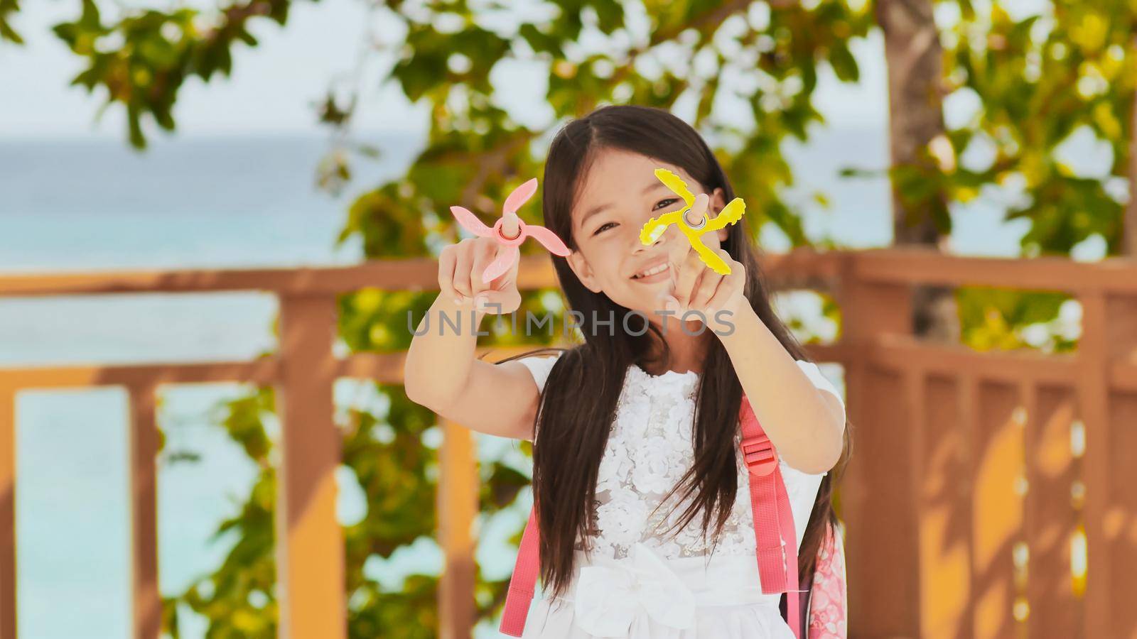 A small filipino schoolgirl shows spinning spinners. Tropical landscape. Summer. Childhood. by DovidPro