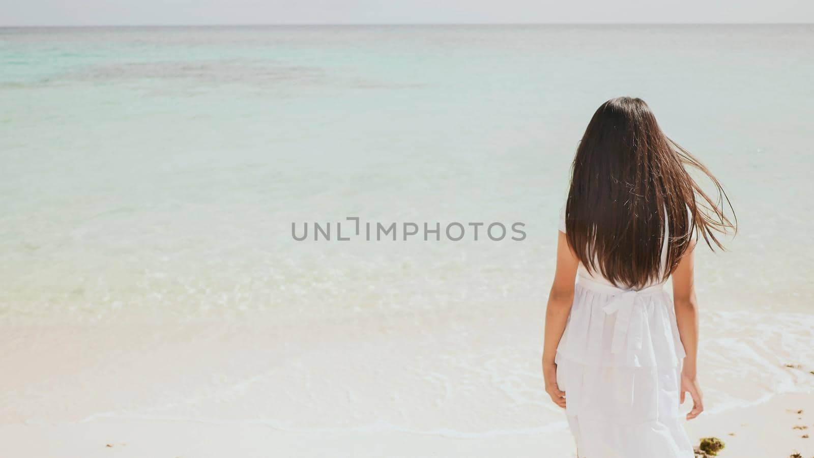 A charming philippine schoolgirl in a white dress is walking along a white sandy beach. Enjoying the tropical scenery. Childhood