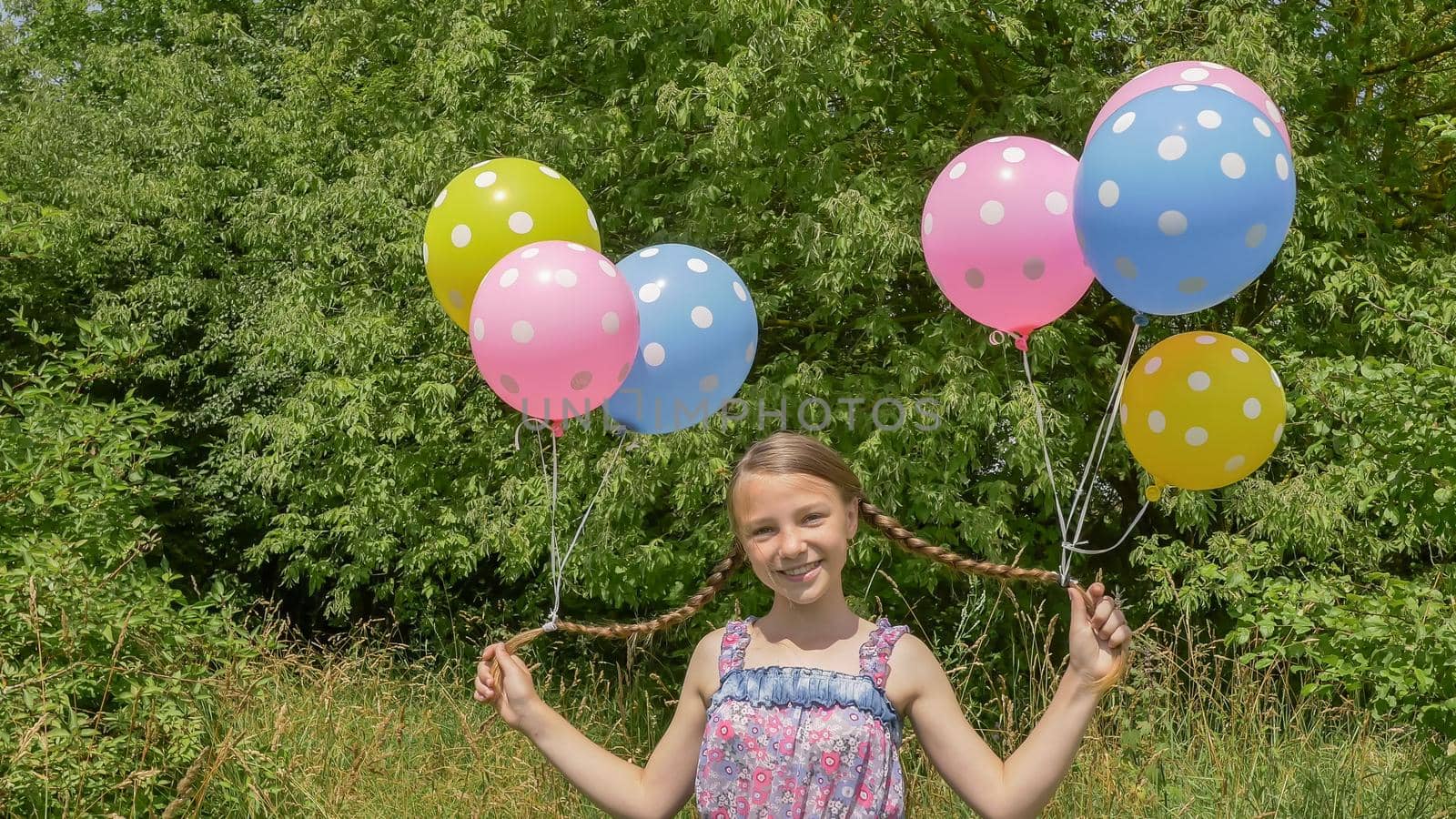 Cheerful and pretty girl with colorful balls attached to her hair and braids on her head. Funny idea with balloons. by DovidPro