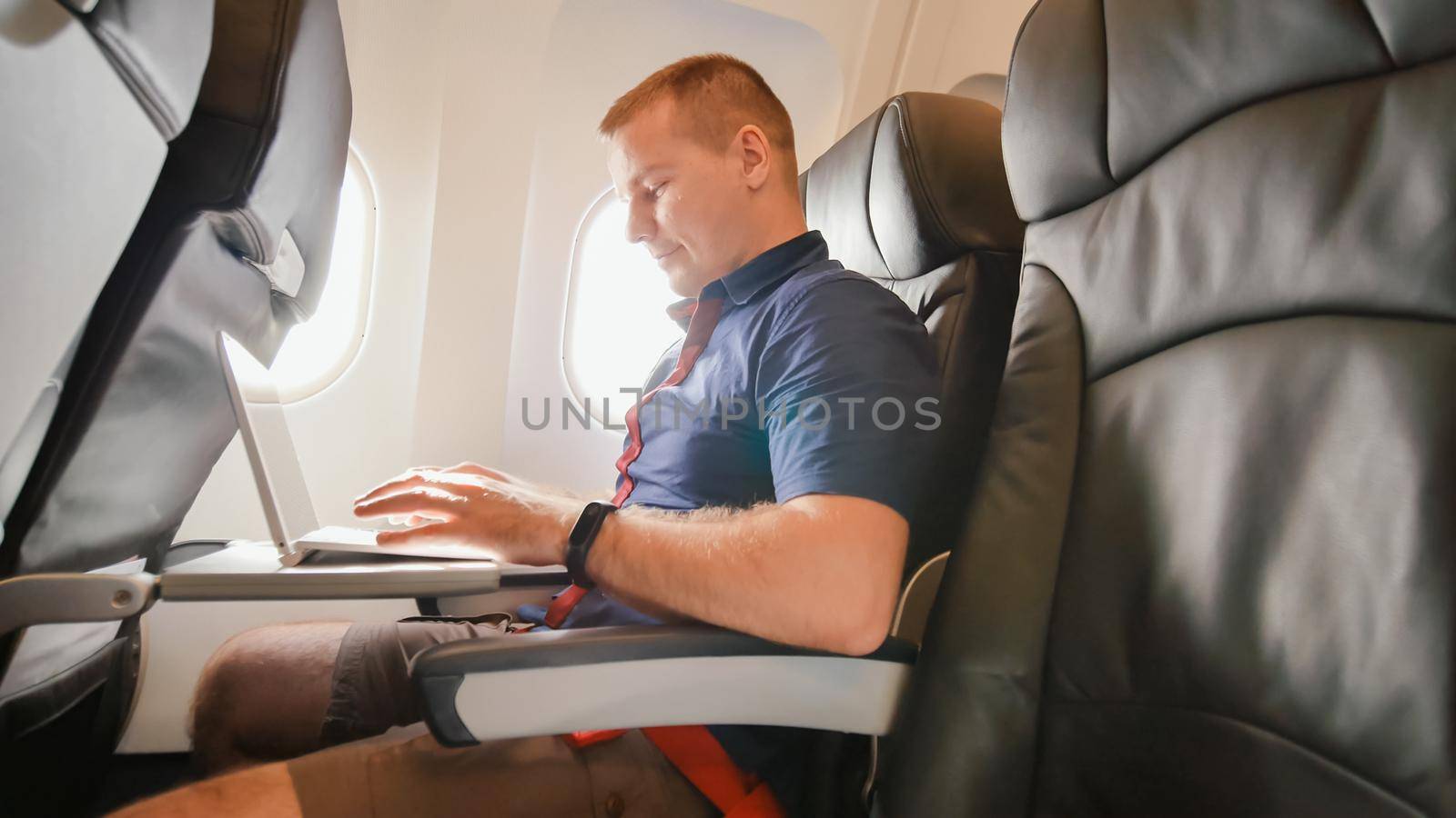 A young man was sitting on the plane and working on his laptop before departure