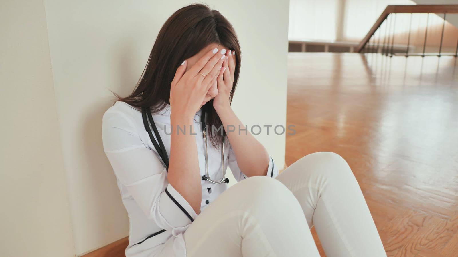 Young girl doctor cries sitting on the floor of the hospital. by DovidPro