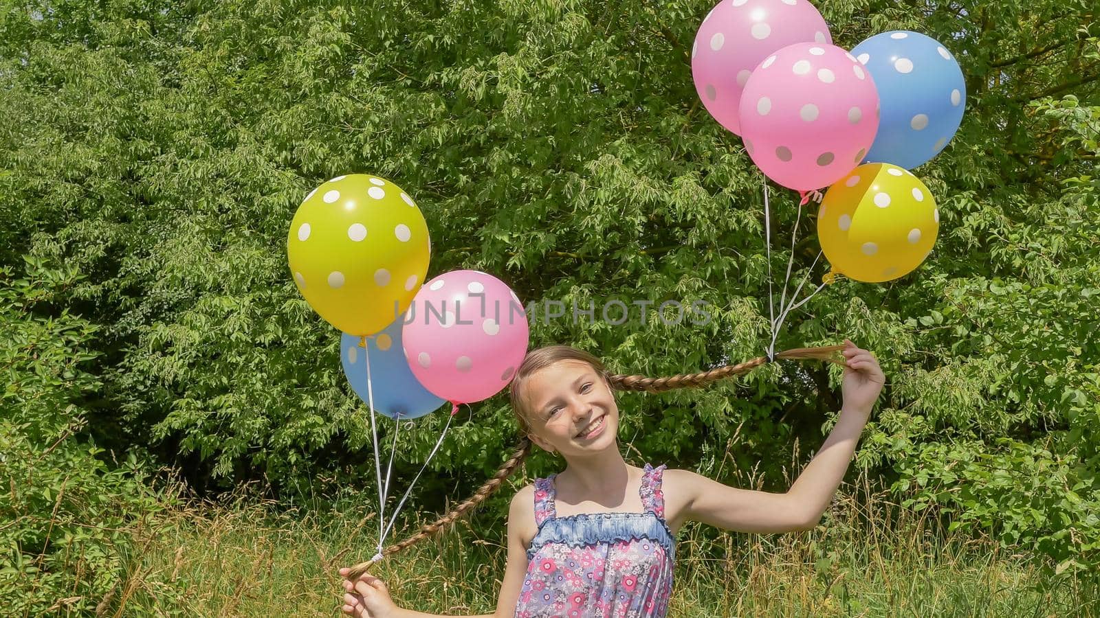 Cheerful and pretty girl with colorful balls attached to her hair and braids on her head. Funny idea with balloons. by DovidPro