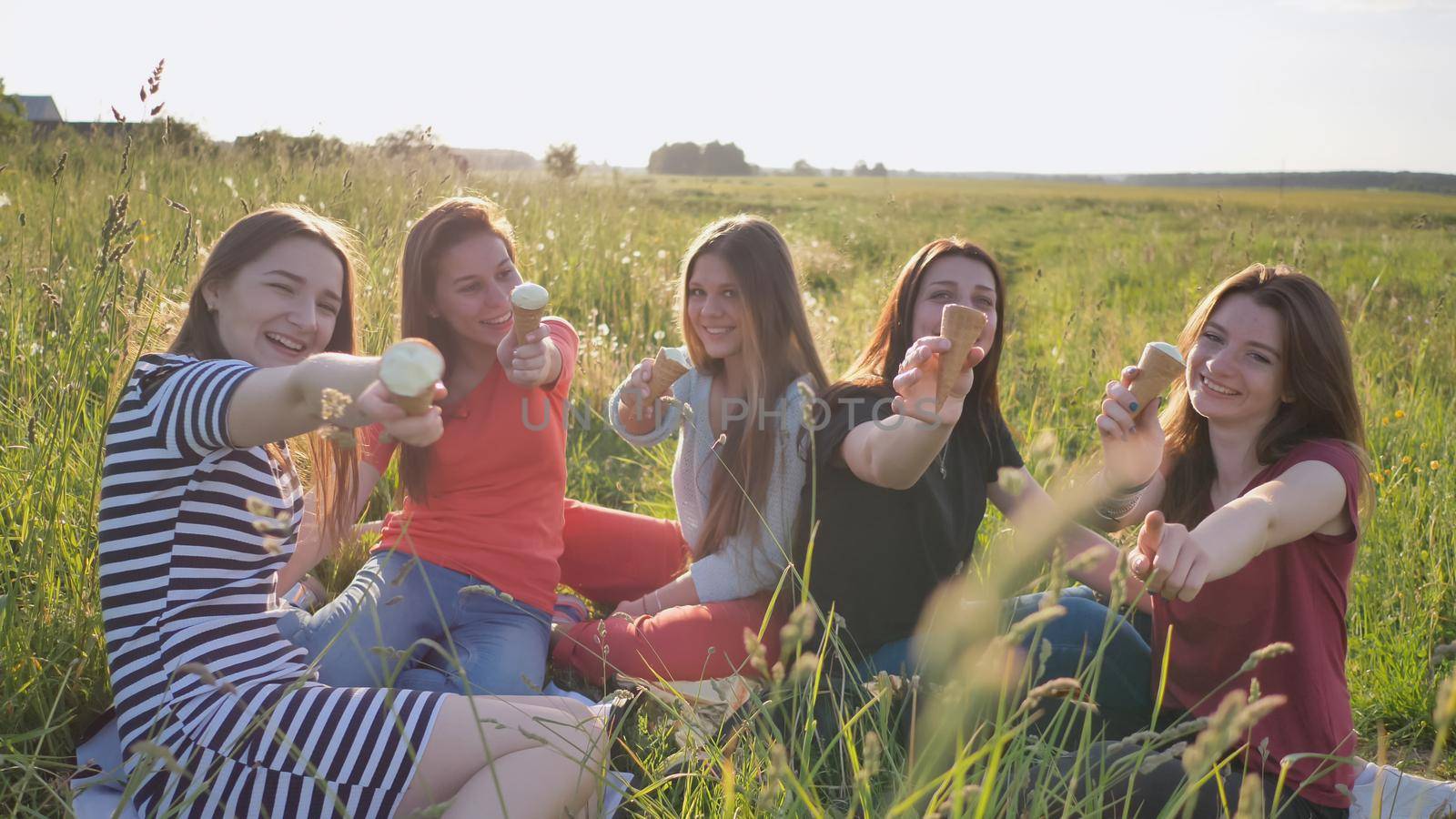 Five young schoolgirls eat ice cream on a meadow on a warm summer day