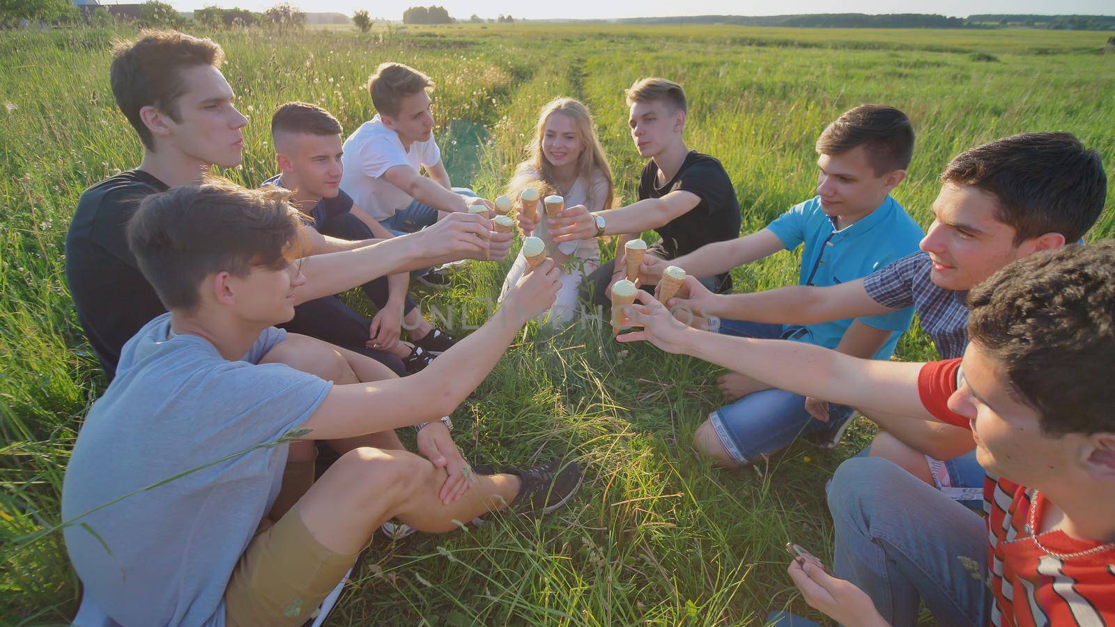 Friends of classmates clink glasses and eat ice cream outdoors in the summer