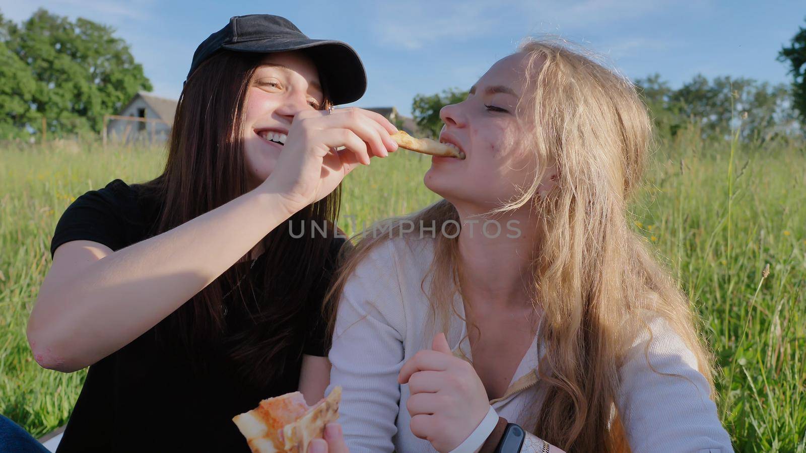 Two girls friends of schoolchildren eat pizza outdoors during the sunset in the evening