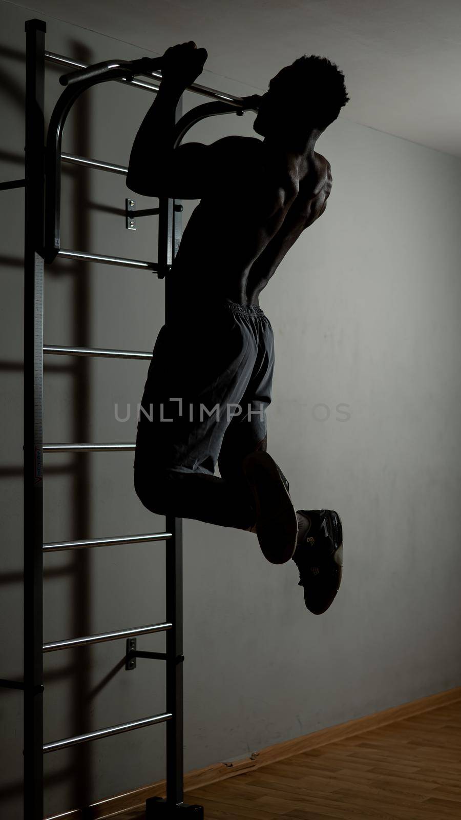 African american man with naked torso pulls up on horizontal bar in gym