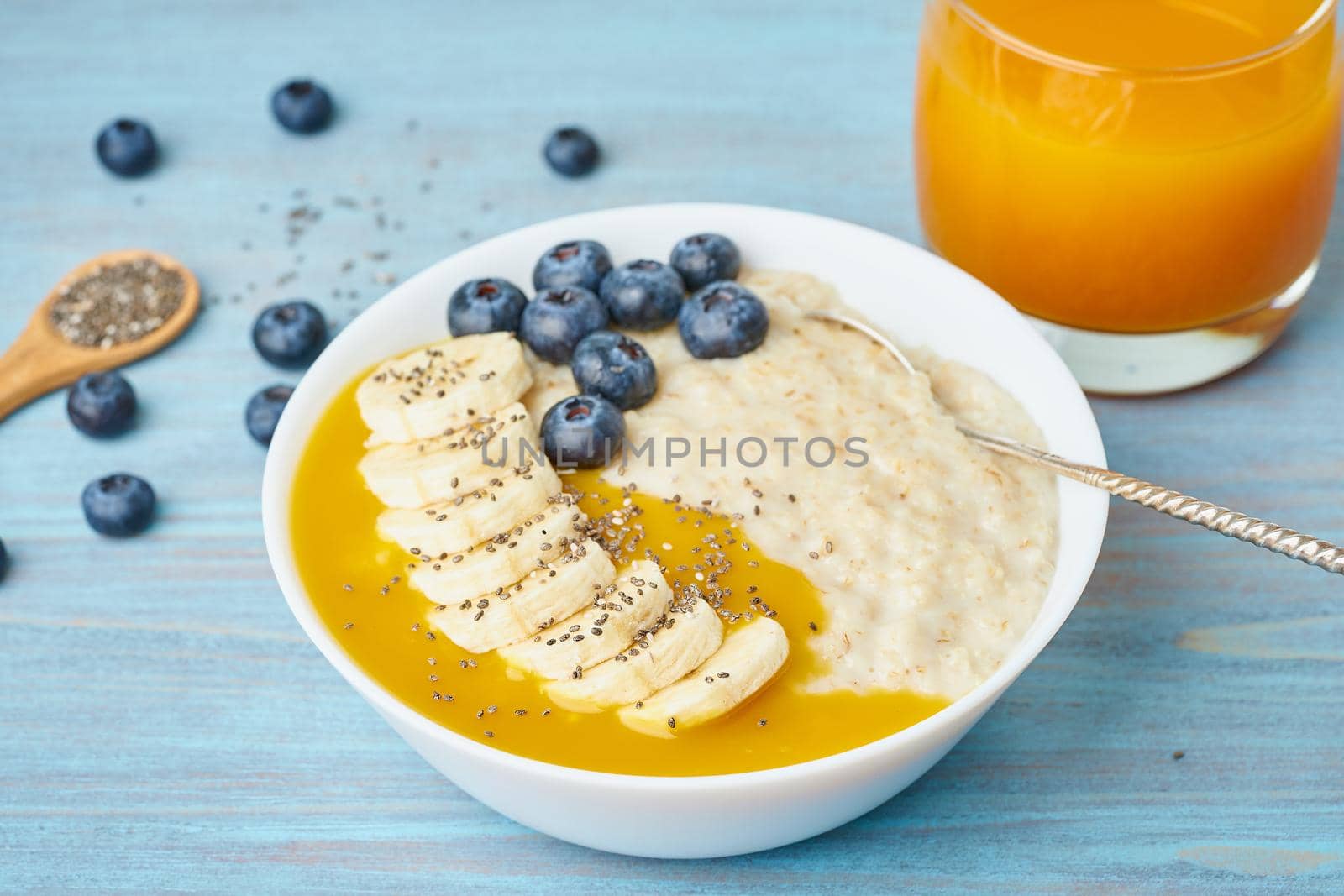 Oatmeal with bananas, blueberries, chia seeds, jam on blue wooden background. Side view, close up. Healthy breakfast. by NataBene