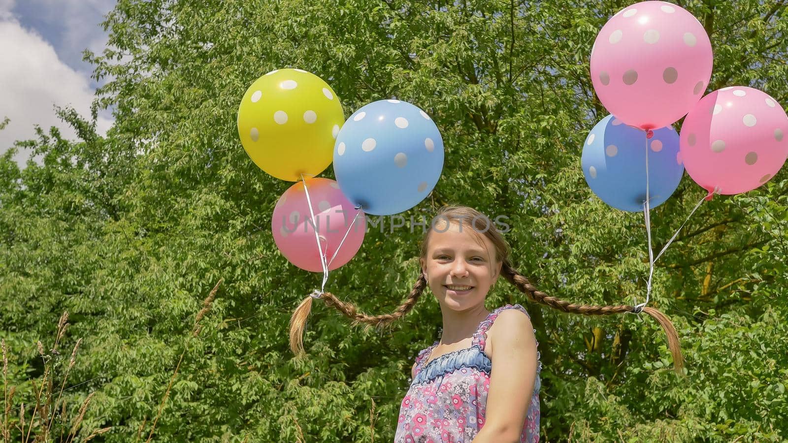 Cheerful and pretty girl with colorful balls attached to her hair and braids on her head. Funny idea with balloons