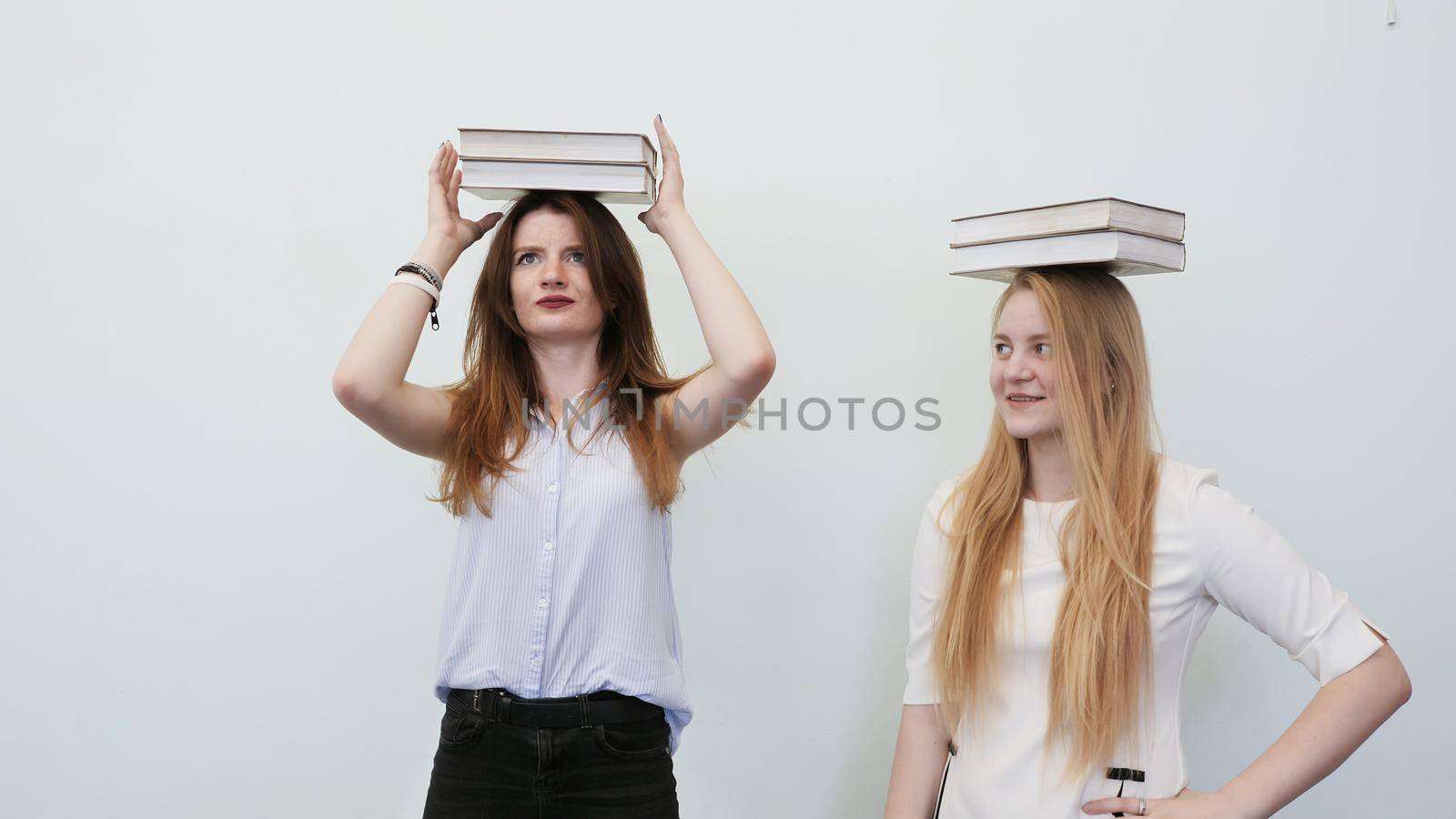 Two schoolgirls play with books holding them on their heads. by DovidPro