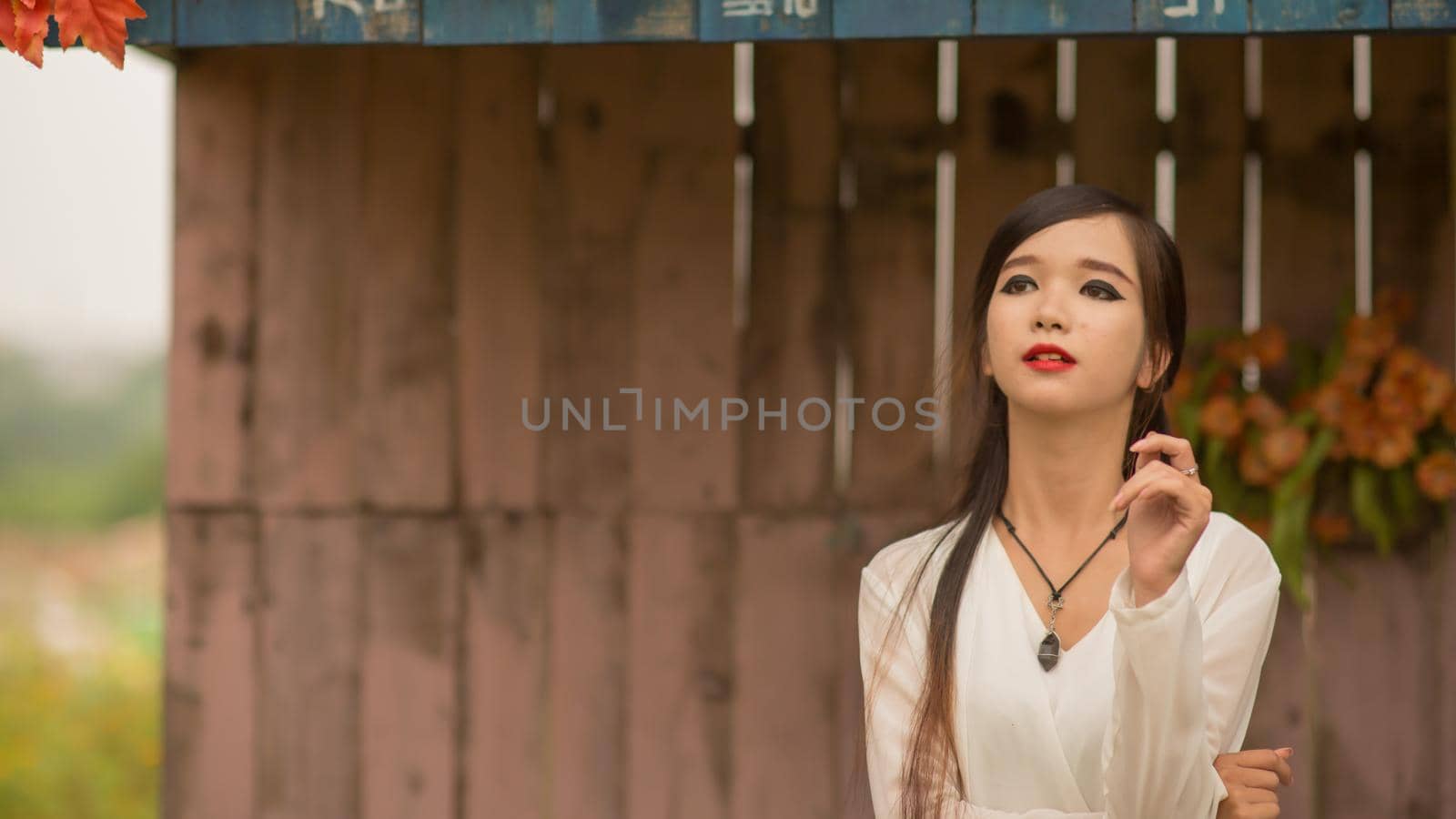 Vietnamese young brunette woman posing against the wall with artificial roses