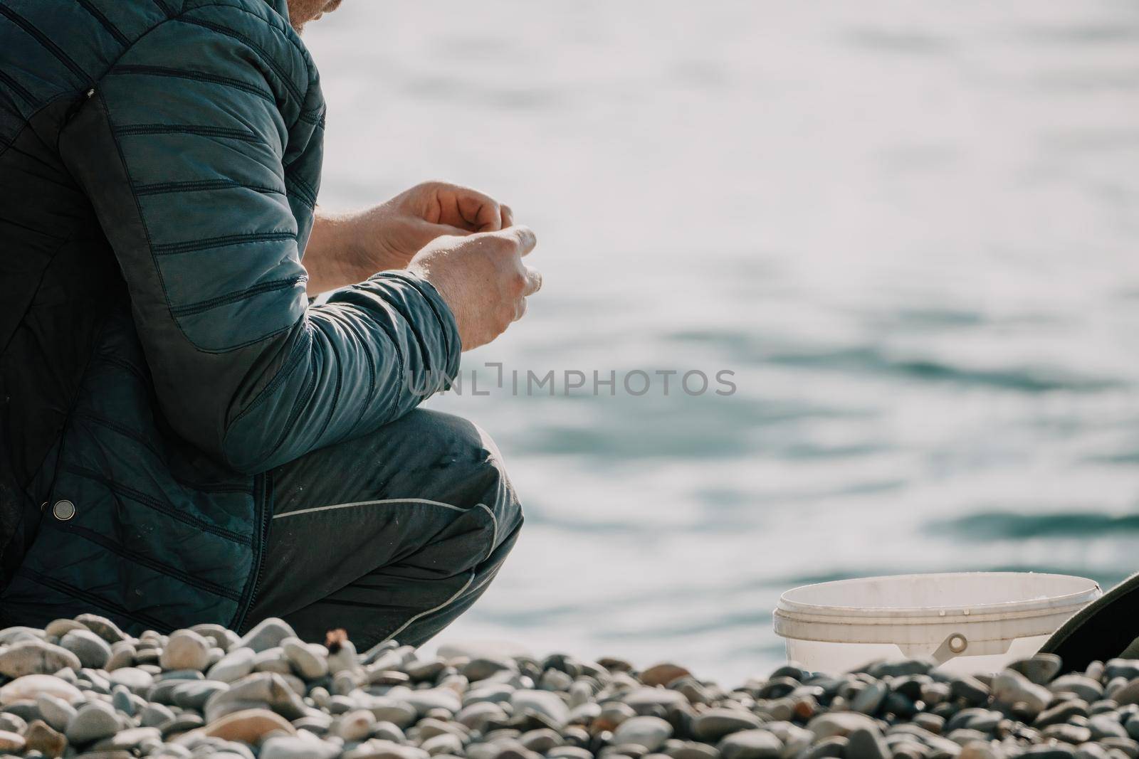 Man hobby fishing on sea tightens a fishing line reel of fish. Calm surface sea. Close-up of a fisherman hands twist reel with fishing line on a rod. Fishing in the blue sea outdoors. by panophotograph