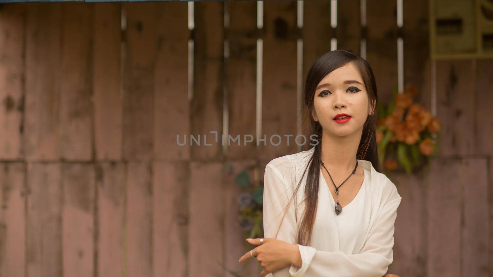 Vietnamese young brunette woman posing against the wall with artificial roses