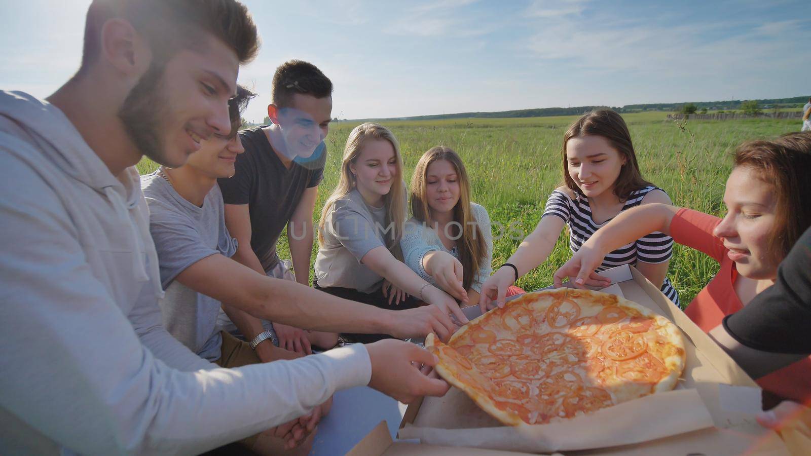 Friends of schoolchildren assort pizza outdoors during the sunset in the evening