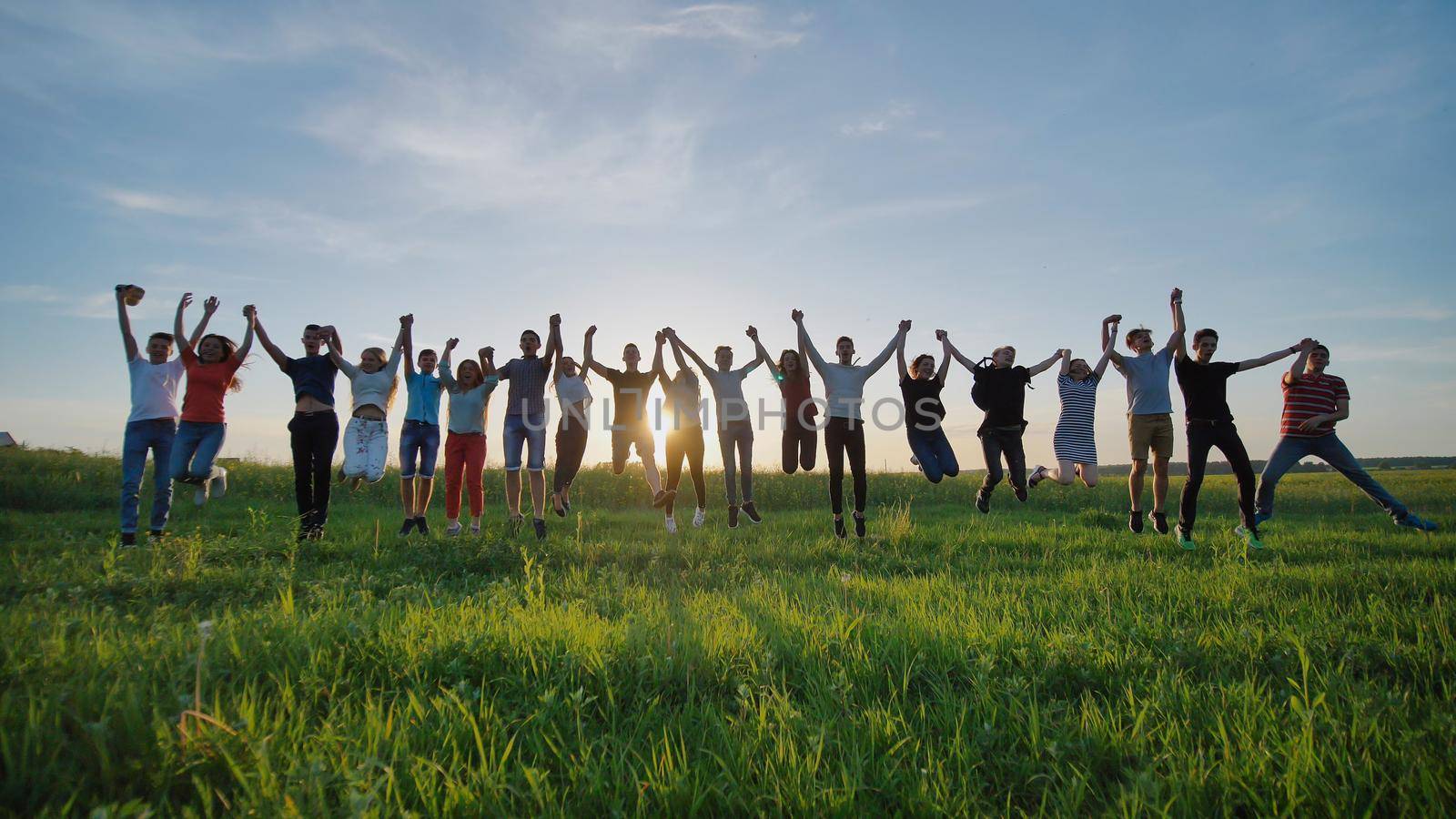 Group of best friends and students jumping outdoors. Sunset with sunshine rays