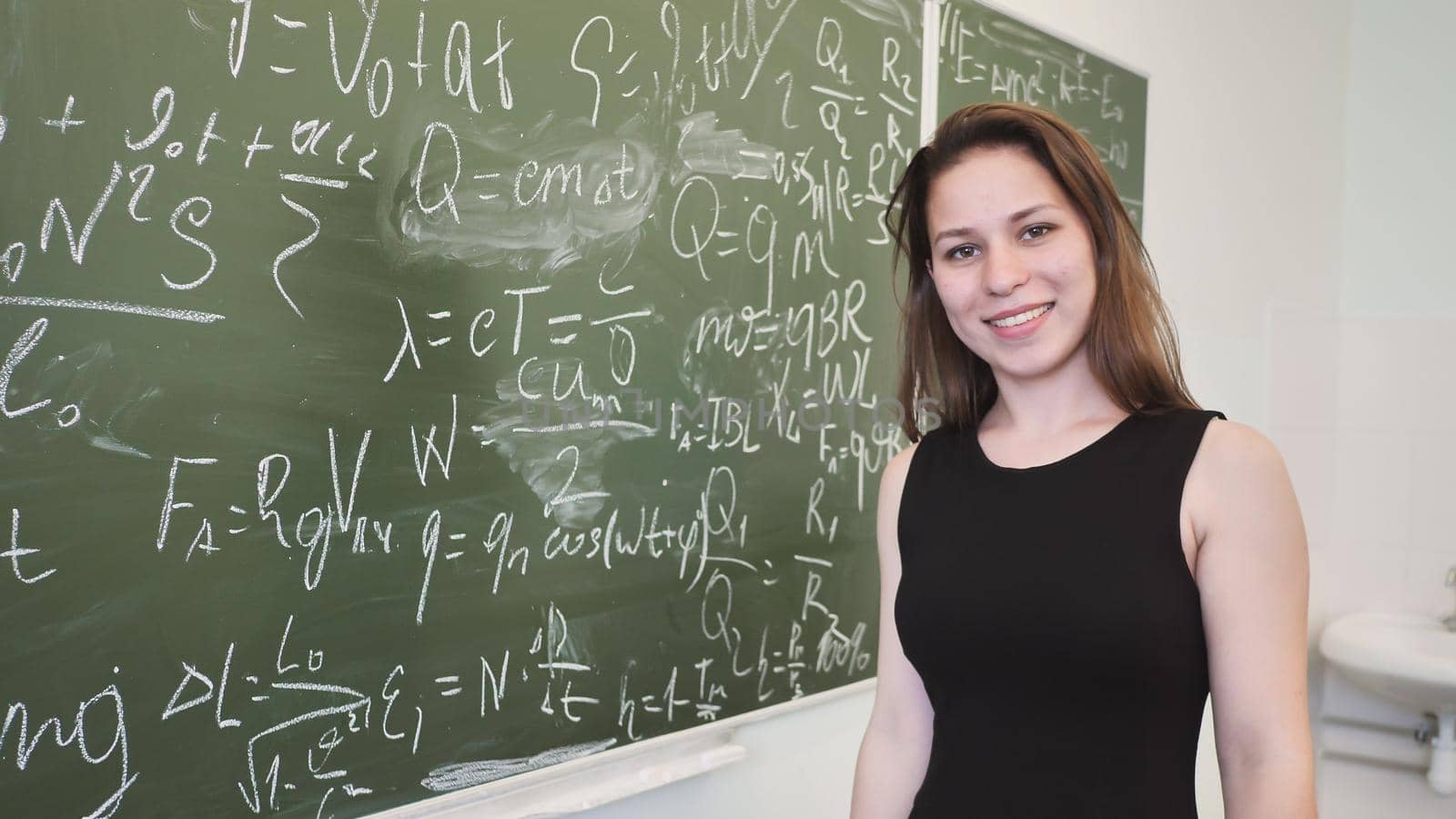 Girl schoolgirl posing on the blackboard a mathematical formula and poses in front of a video camera.