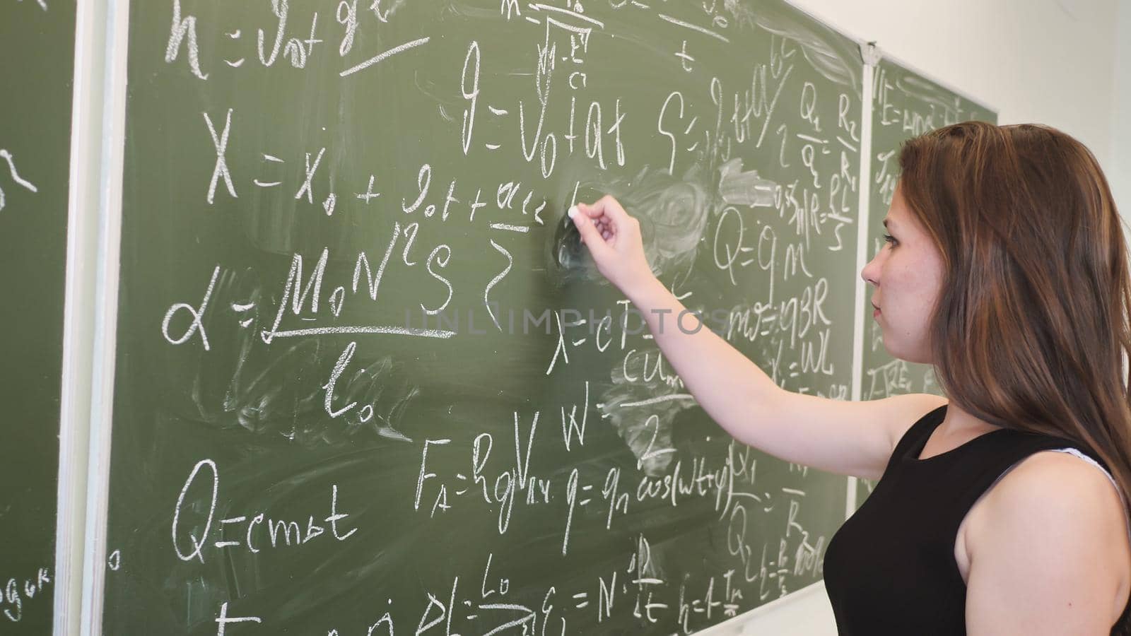 Girl schoolgirl writes on the blackboard a mathematical formula and poses in front of a video camer
